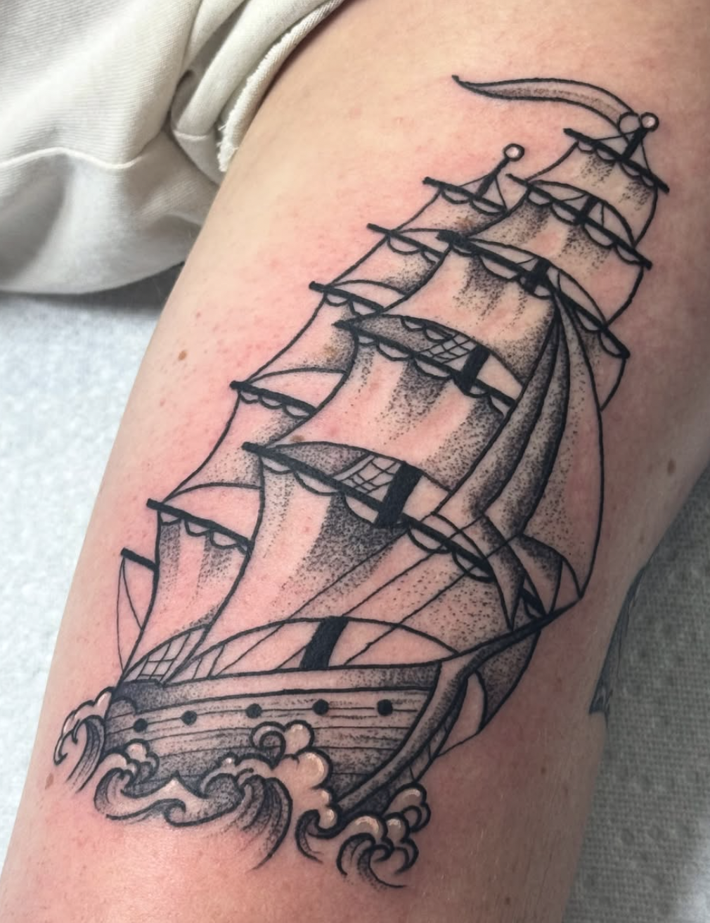 A black-and-gray tattoo of a sailing ship on the skin.