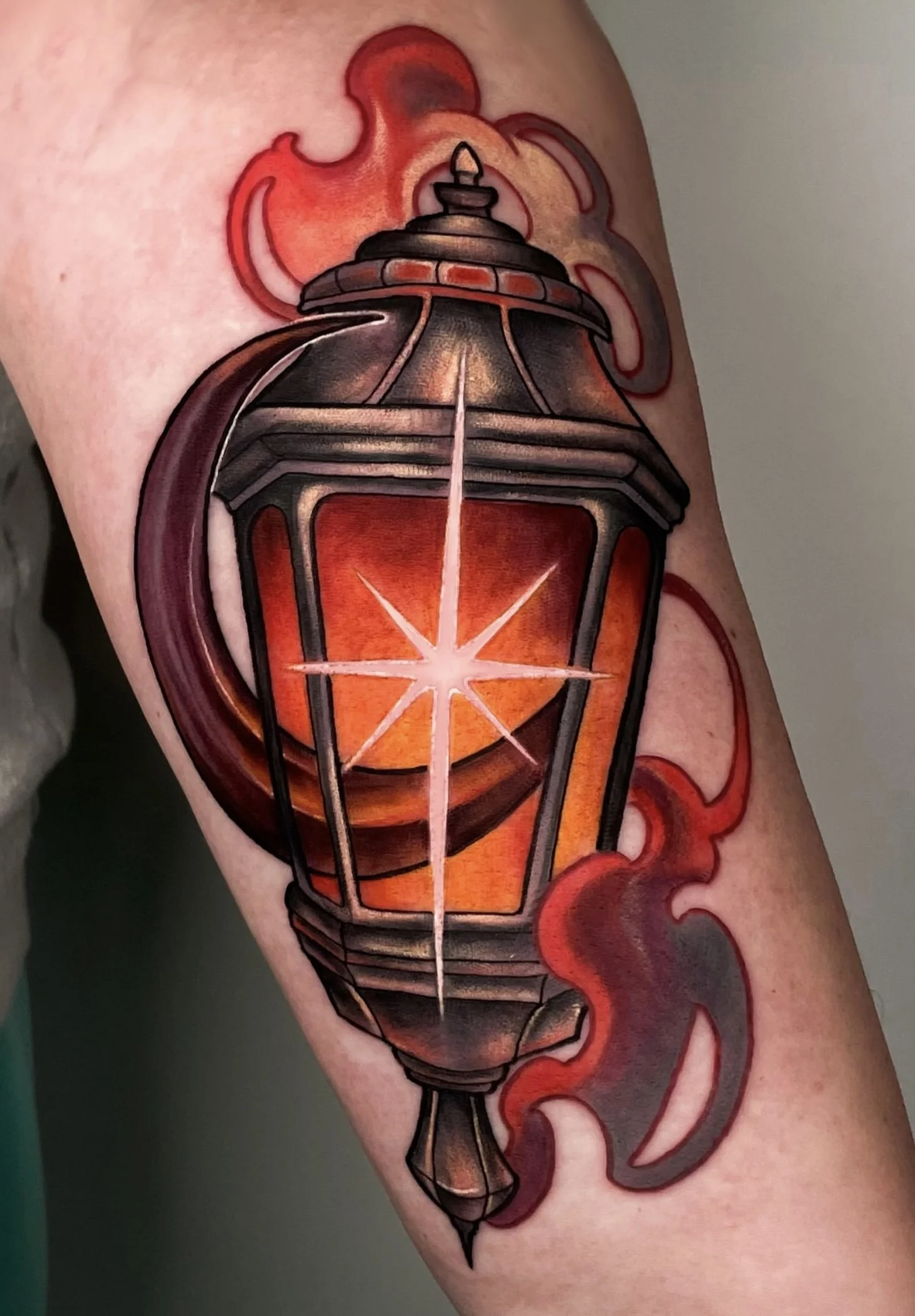Tatouage d'une lanterne orange avec des éléments noirs et rouges sur le bras.