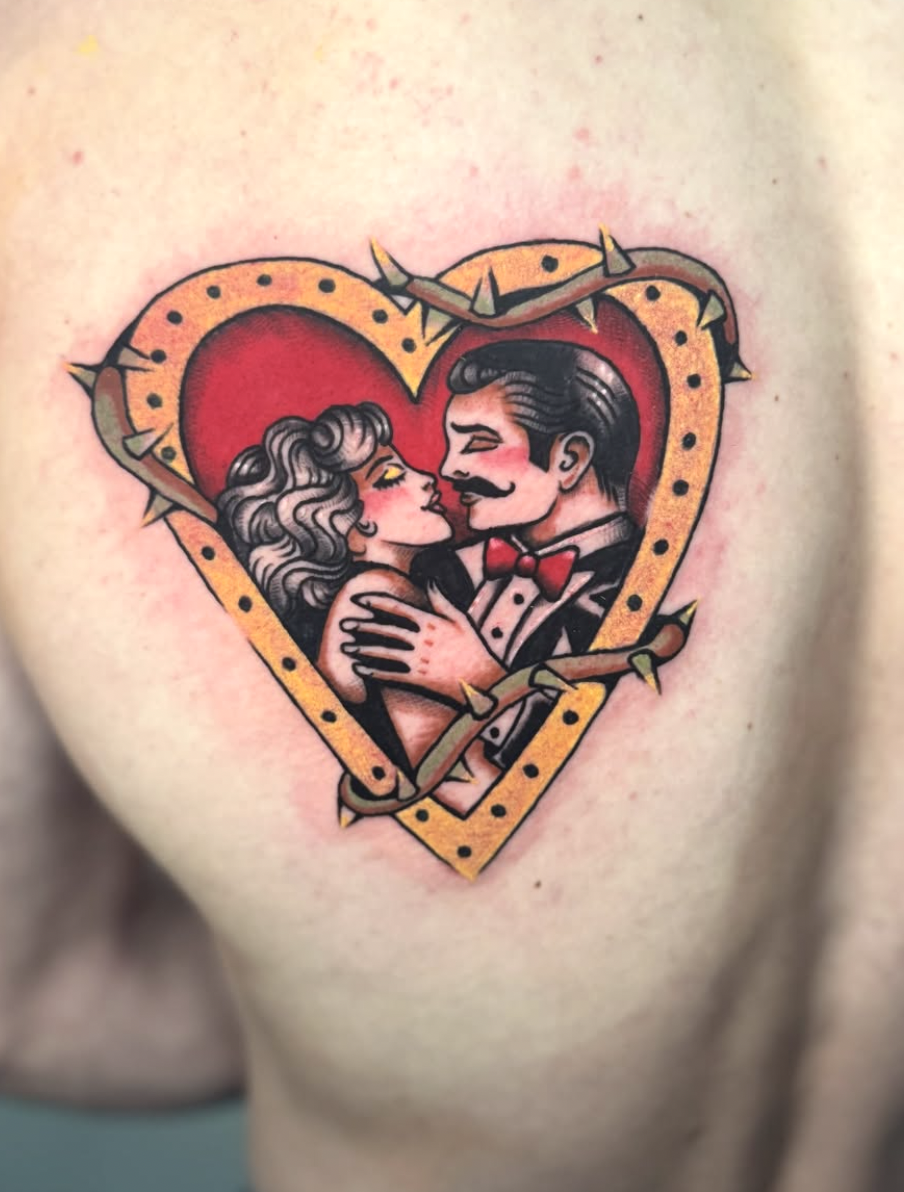 A tattoo depicting a couple in formal attire kissing in the center of a heart surrounded by barbed wire and spikes, in a traditional style.