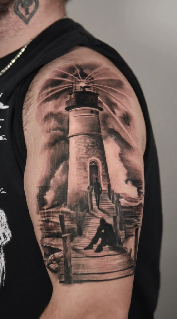 Black and white tattoo of a lighthouse with a wooden walkway and two people in front, emitting light and beams into the sky.