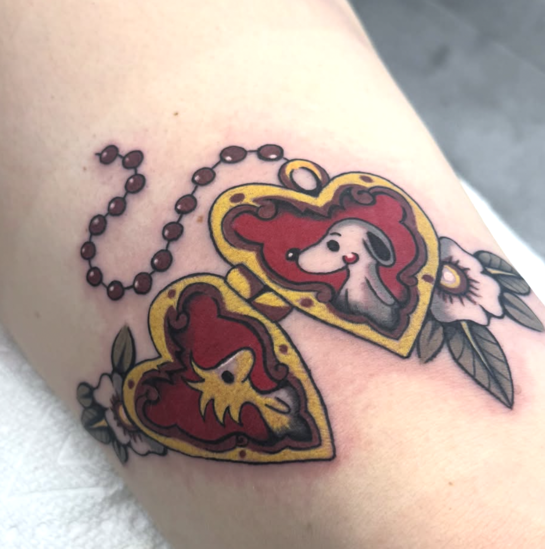 A tattoo of two hearts with a stylized dog inside, surrounded by flowers and leaves, in a traditional style.