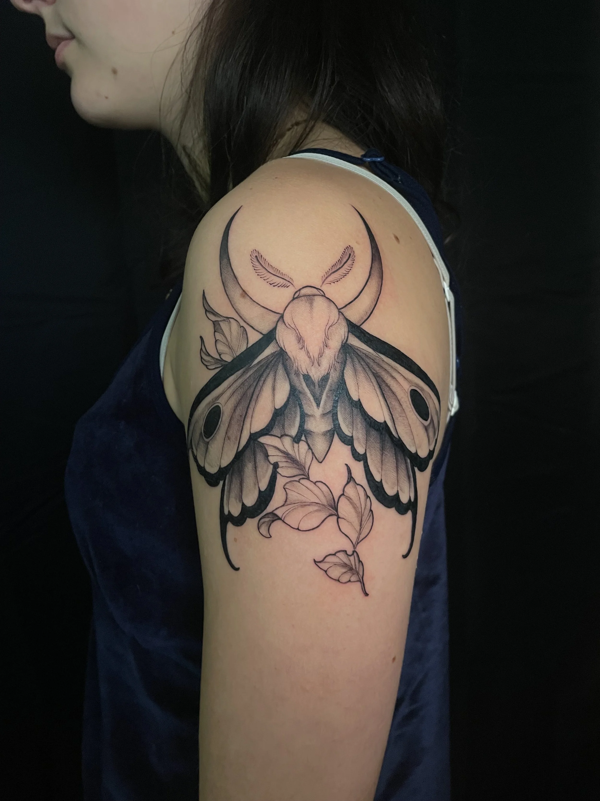 Tatouage d'une grande papillon avec des feuilles suspendues, sur l'épaule d'une femme.