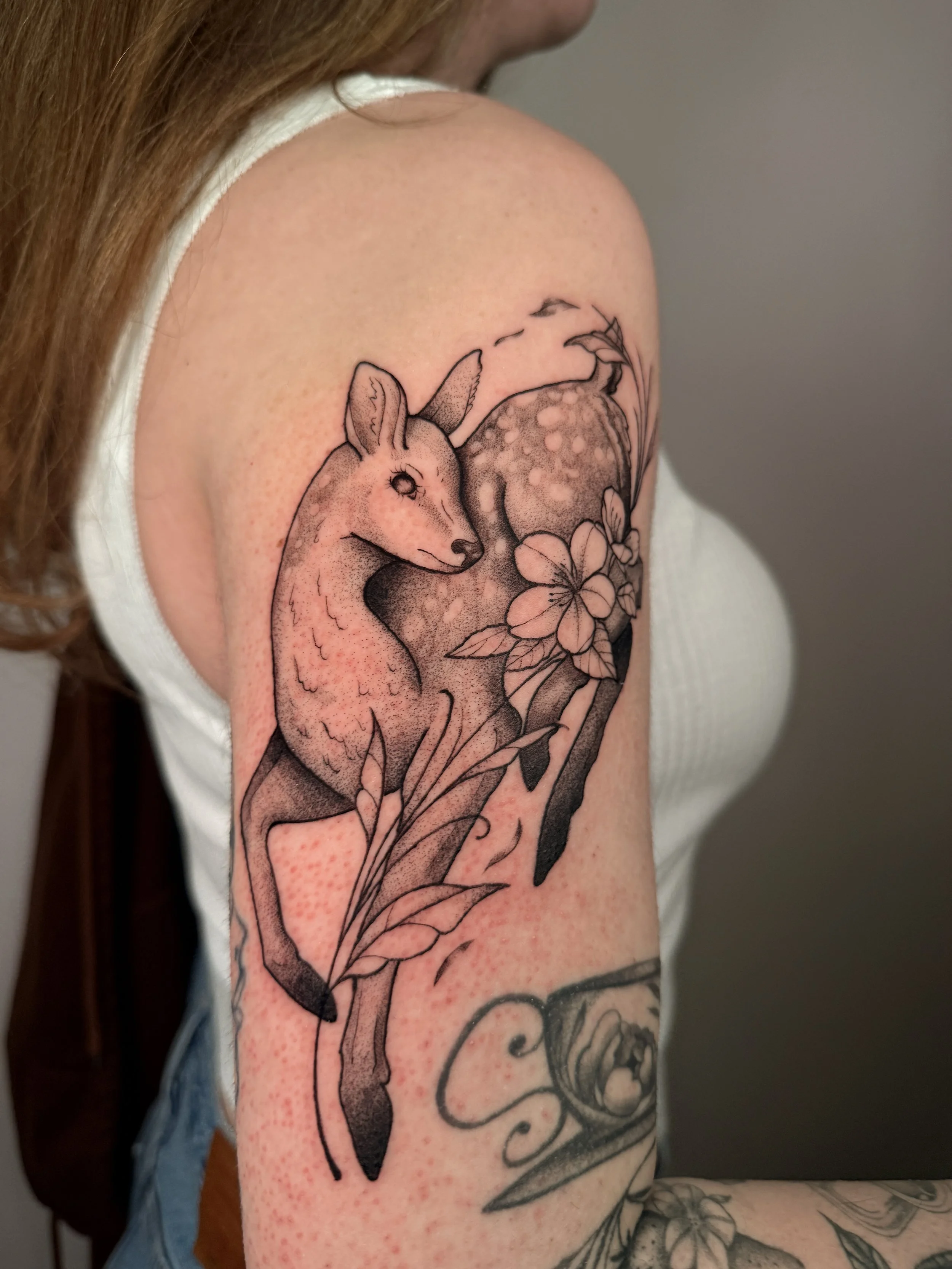 A tattoo of a deer with flowers on someone's arm.