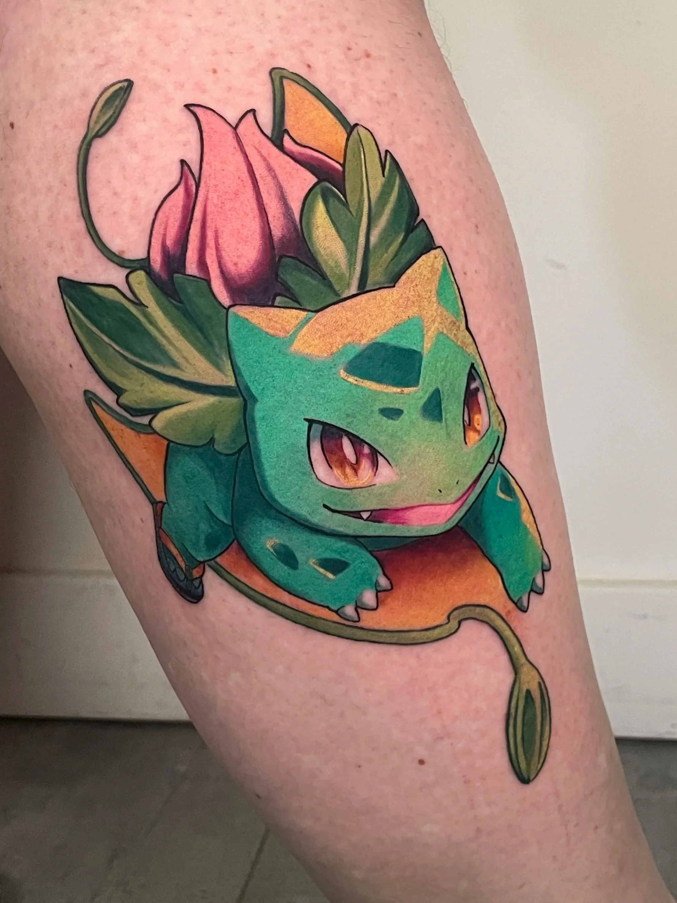 Tatouage coloré représentant un Pokémon, essentiellement un Bulbizarre, sur le bras d'une personne.