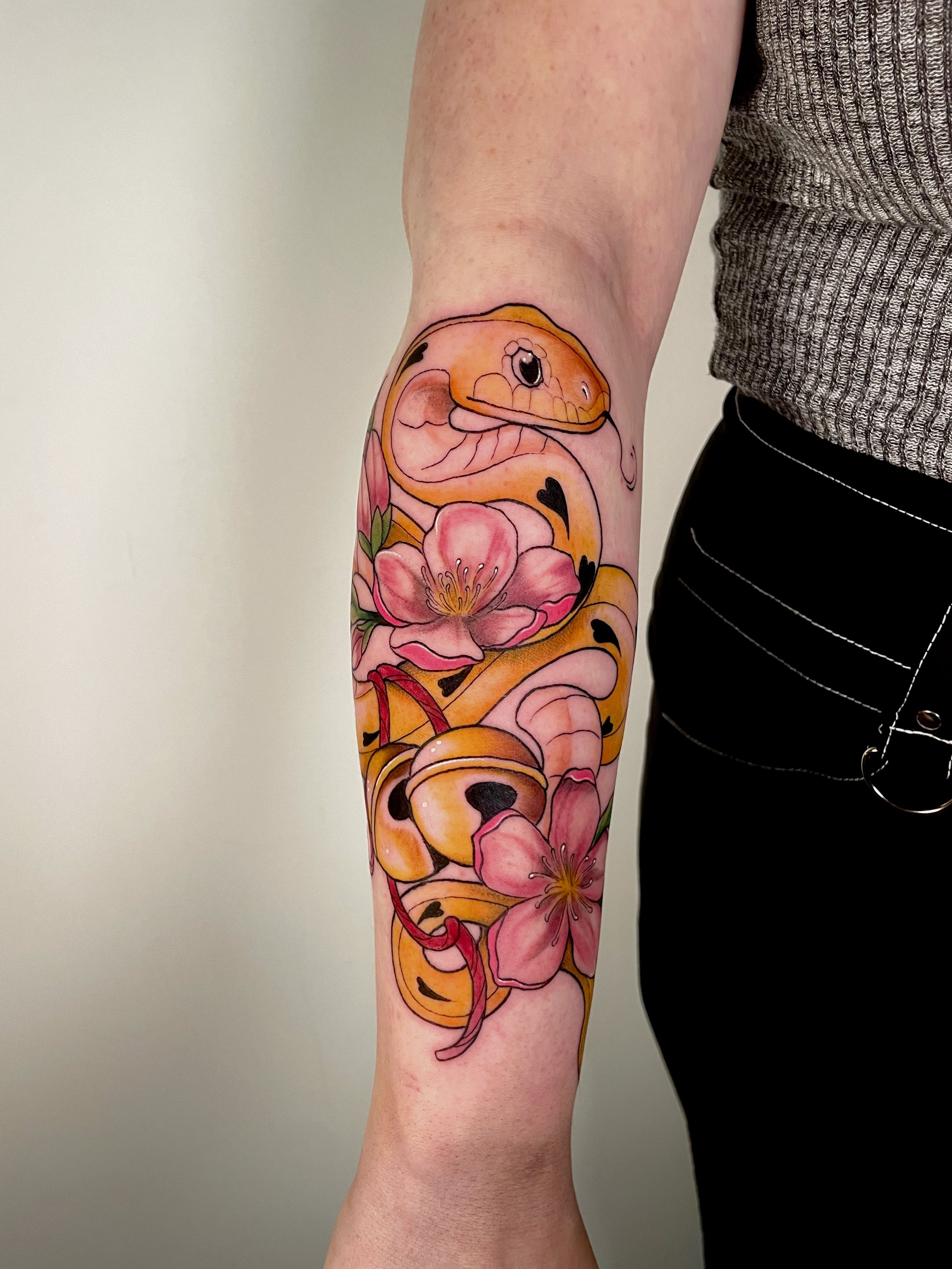 Colorful tattoo of a snake surrounding pink flowers on a person's arm.