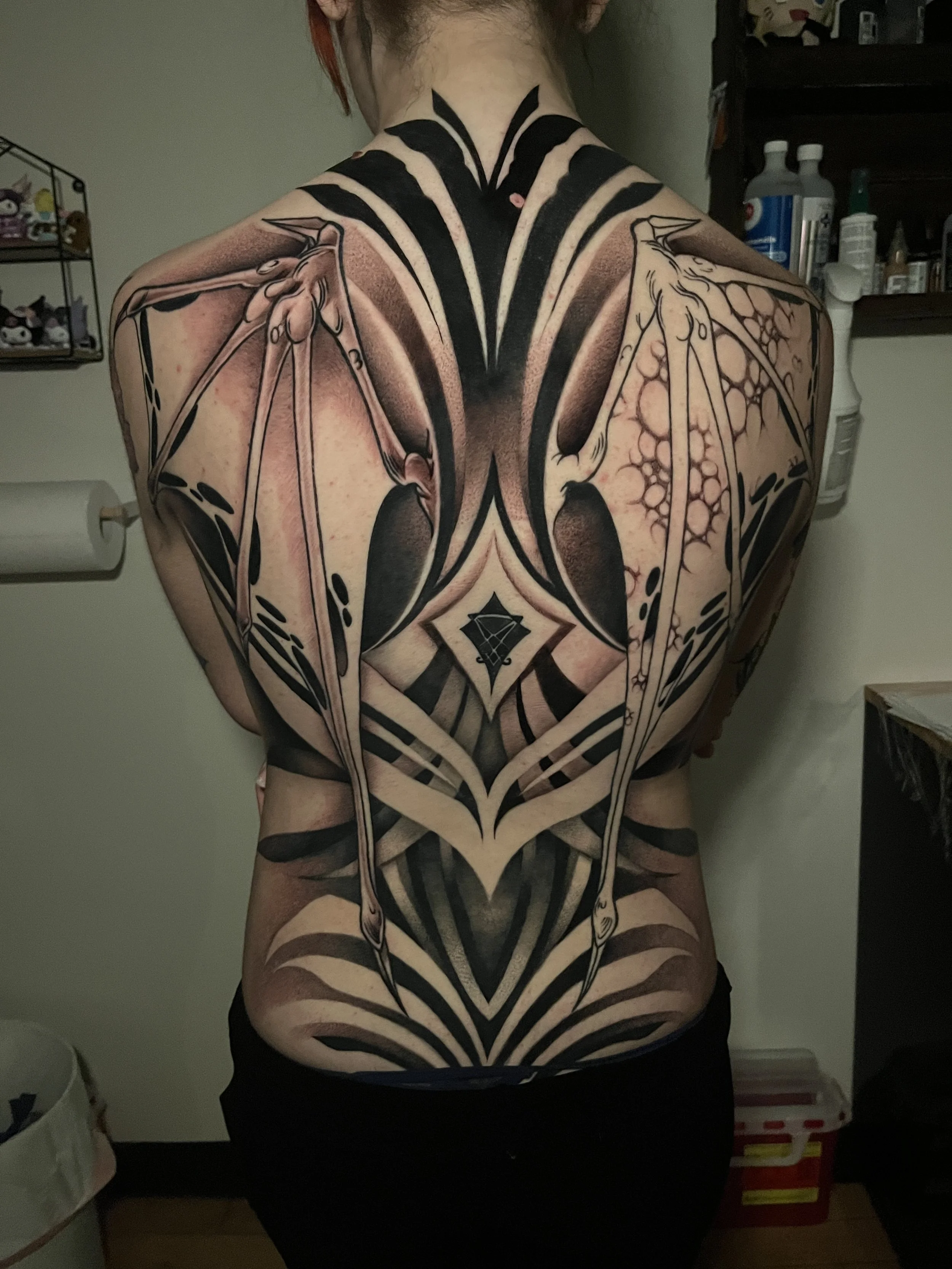 Black and gray tattoo in a geometric and abstract style covering the back of a person, with clean lines, symmetrical shapes, and a central motif evoking a diamond or a stylized star.
