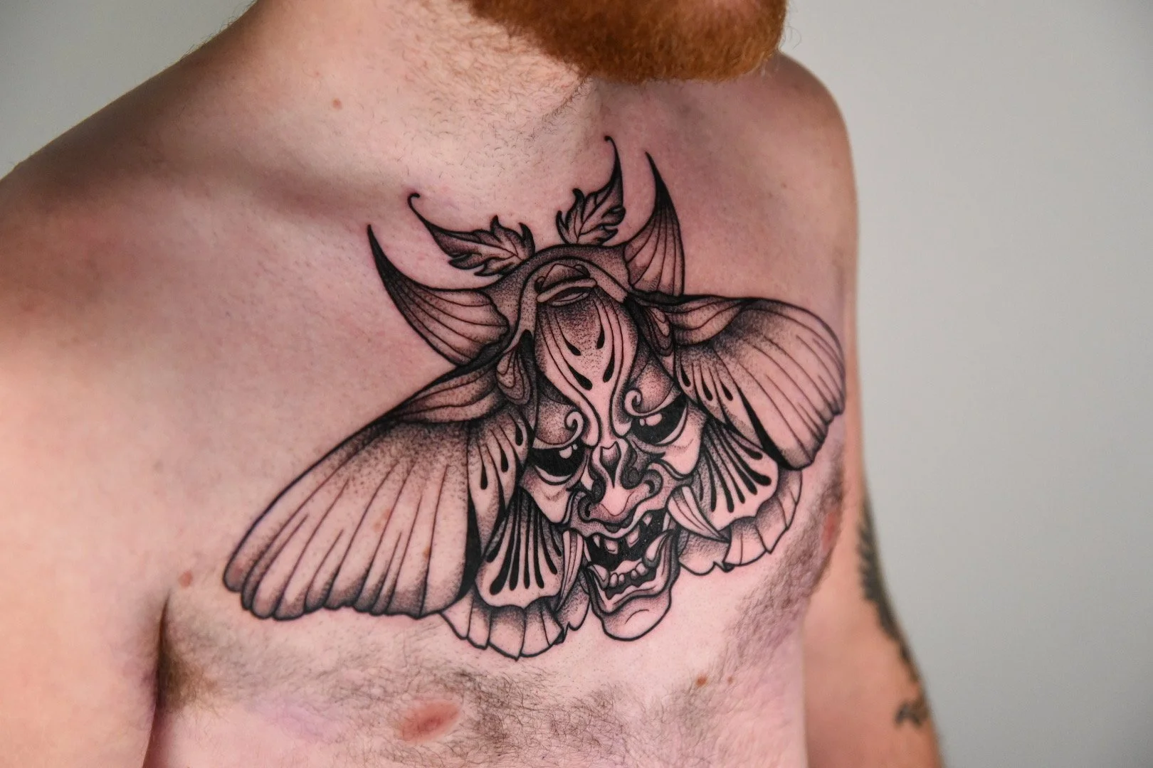 Tattoo of a magic lantern on a man's torso, with black and gray details, depicting a fantastic face with an intense expression.