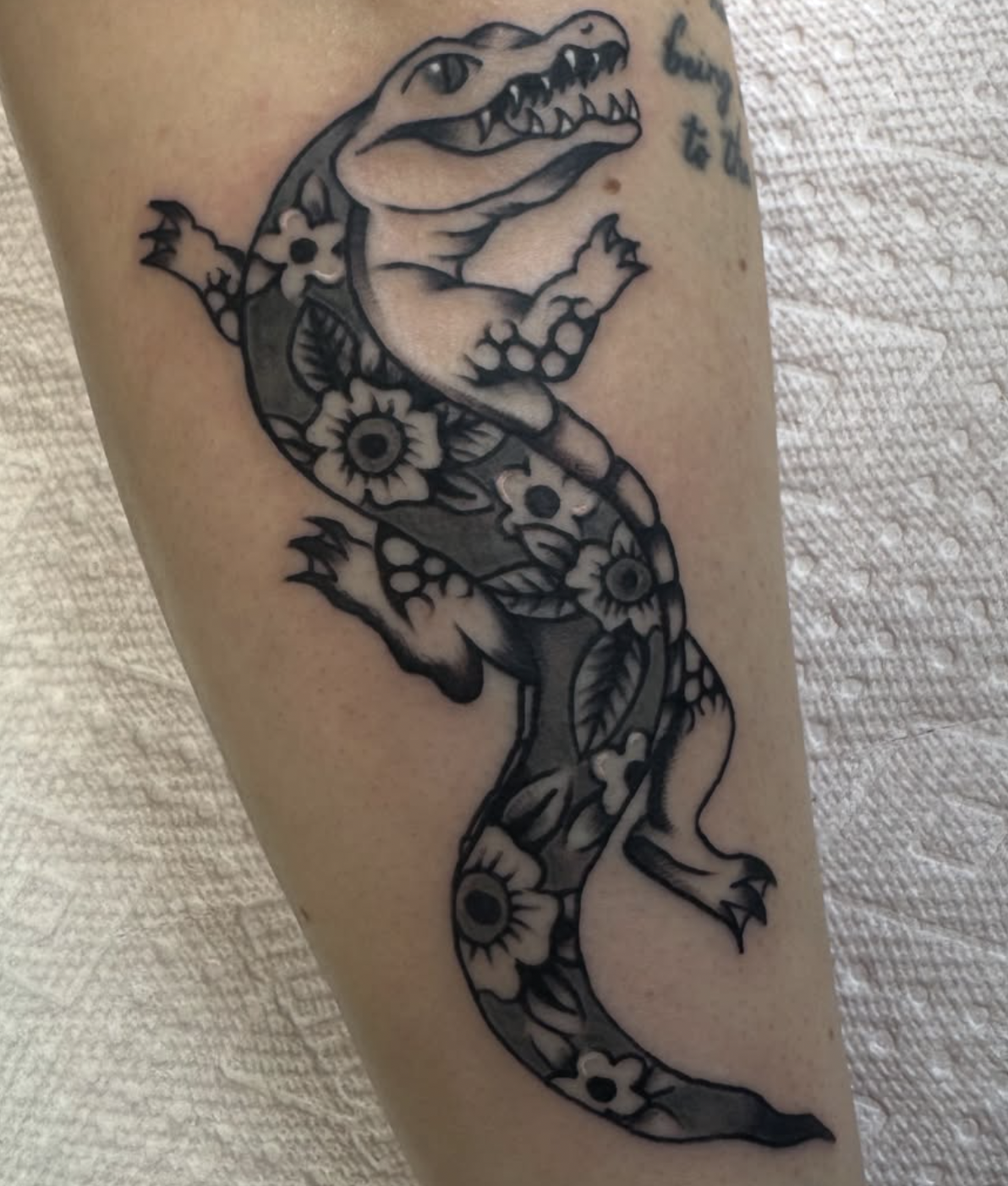 A black tattoo of a crocodile with flowers and leaves.