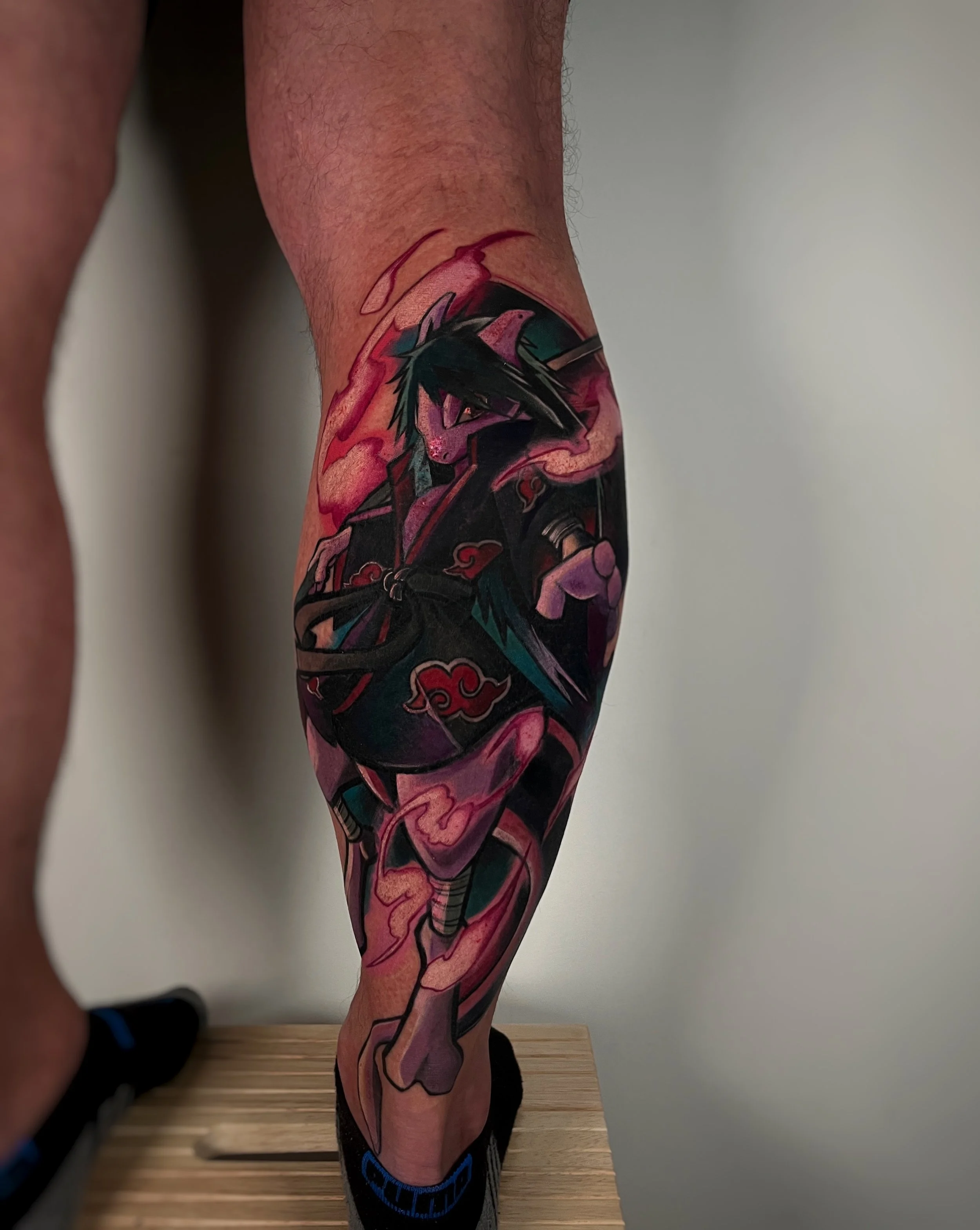 A colorful tattoo depicting a manga or anime character on a leg, featuring graphic design elements and bright colors.