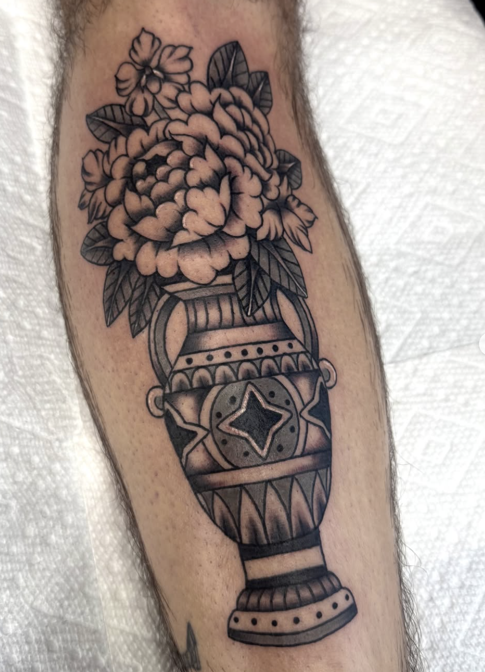 A tattoo of a vase containing flowers, with geometric patterns and details in black and gray, on an arm.