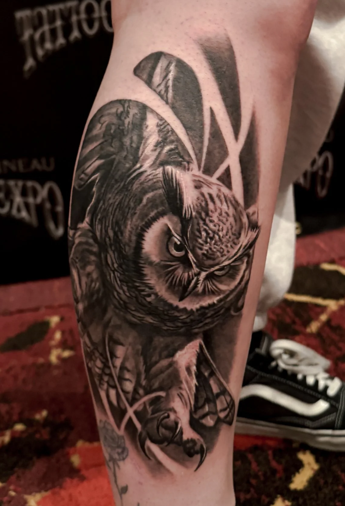 Black and gray tattoo of an owl with realistic details, combined with an abstract geometric pattern in the background.