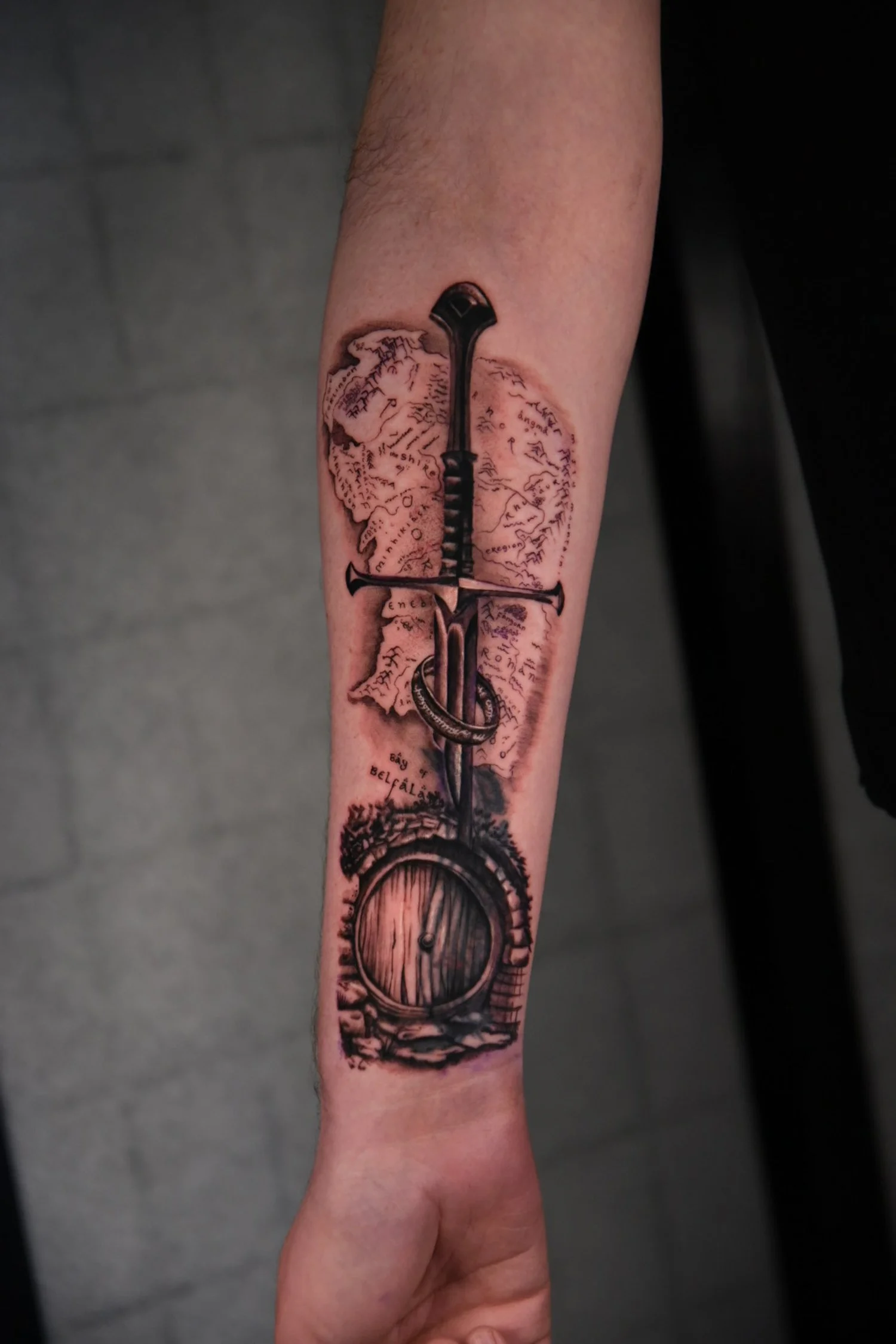 Tattoo of a sword pierced in the arm with a stylized map in the background, a barrel at the bottom.