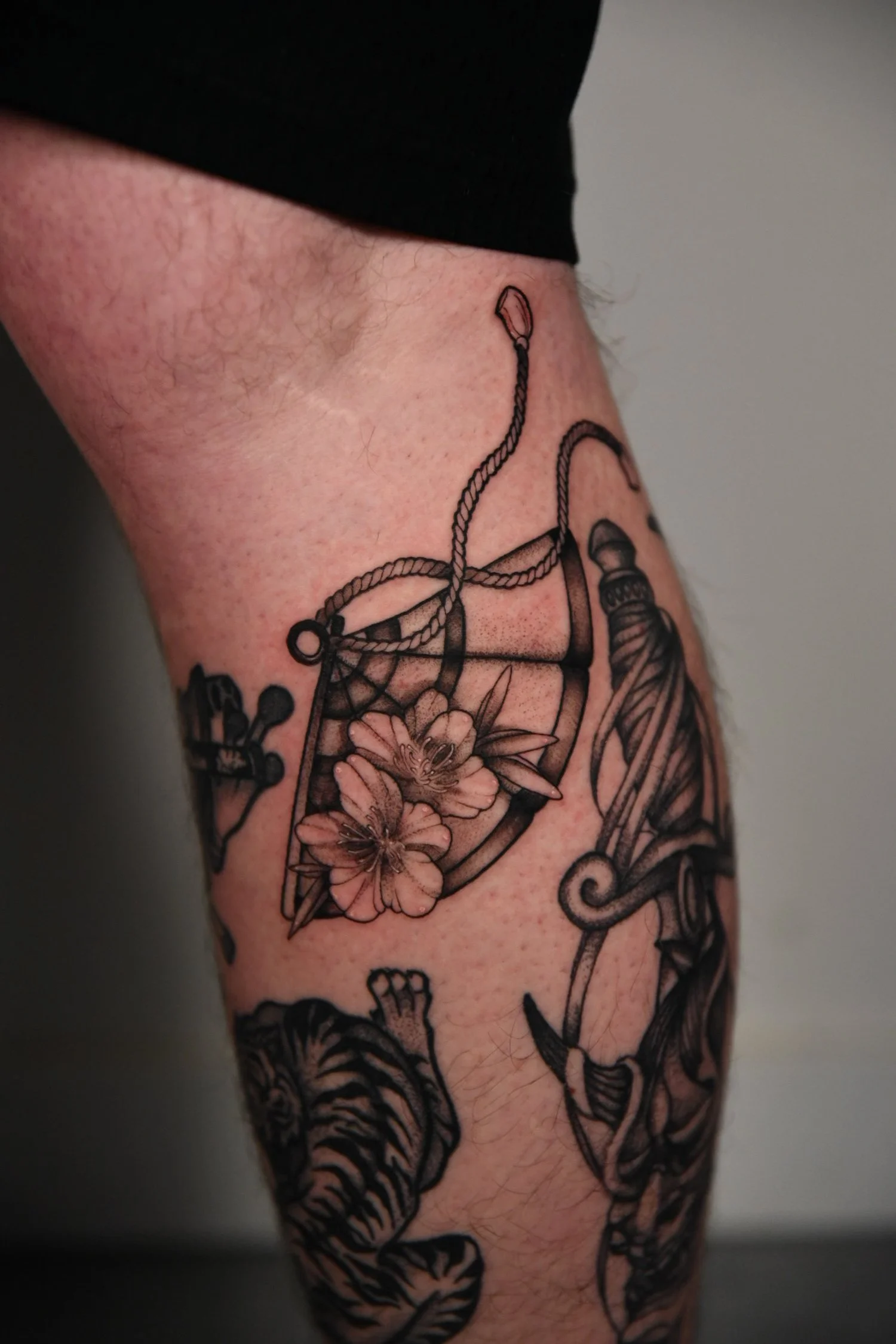 Tatouage d'une boîte de pêche avec des fleurs et des éléments de pêche sur la cuisse.