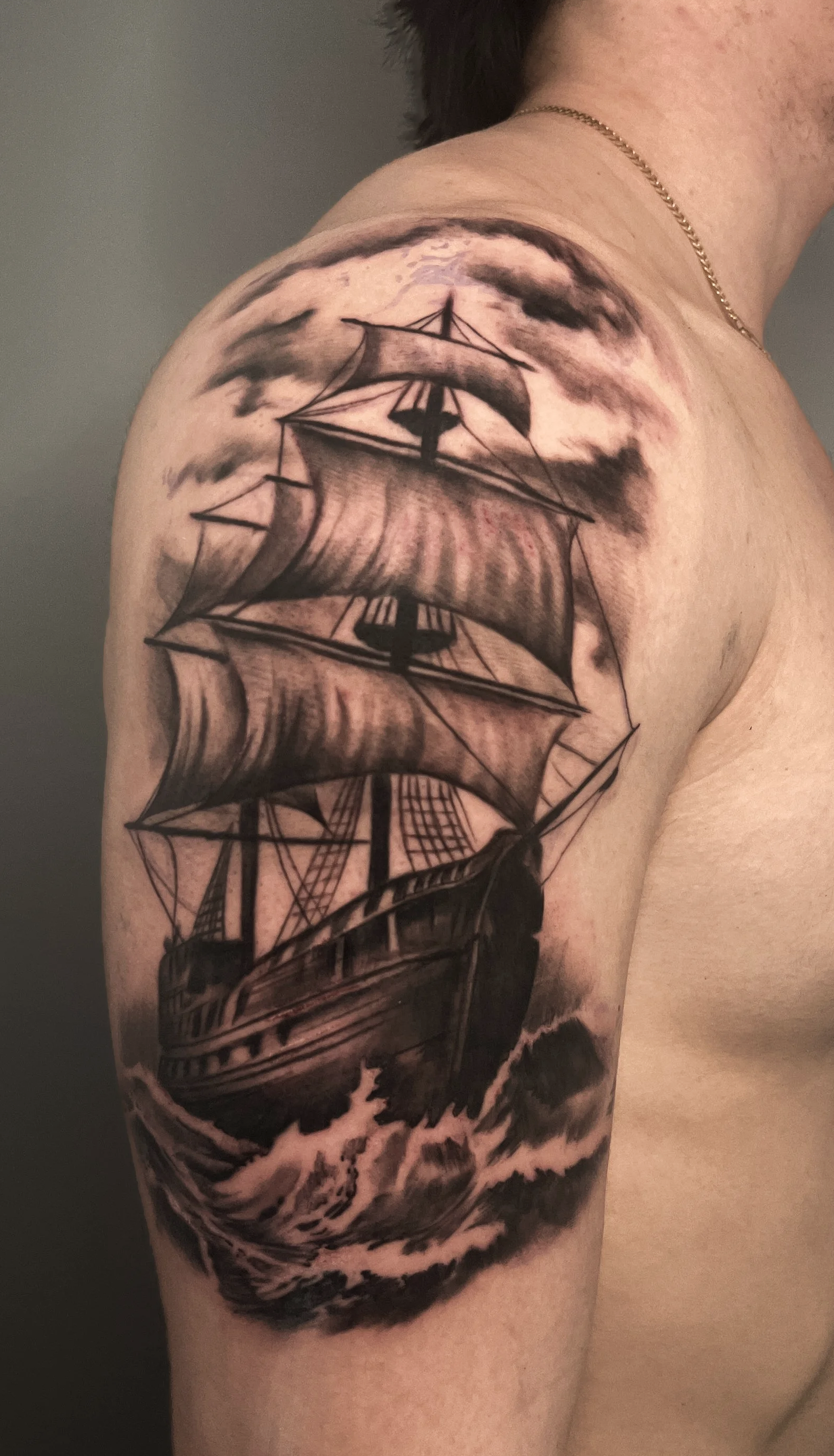 Black and gray tattoo of an old sailing ship at sea, with clouds in the background.