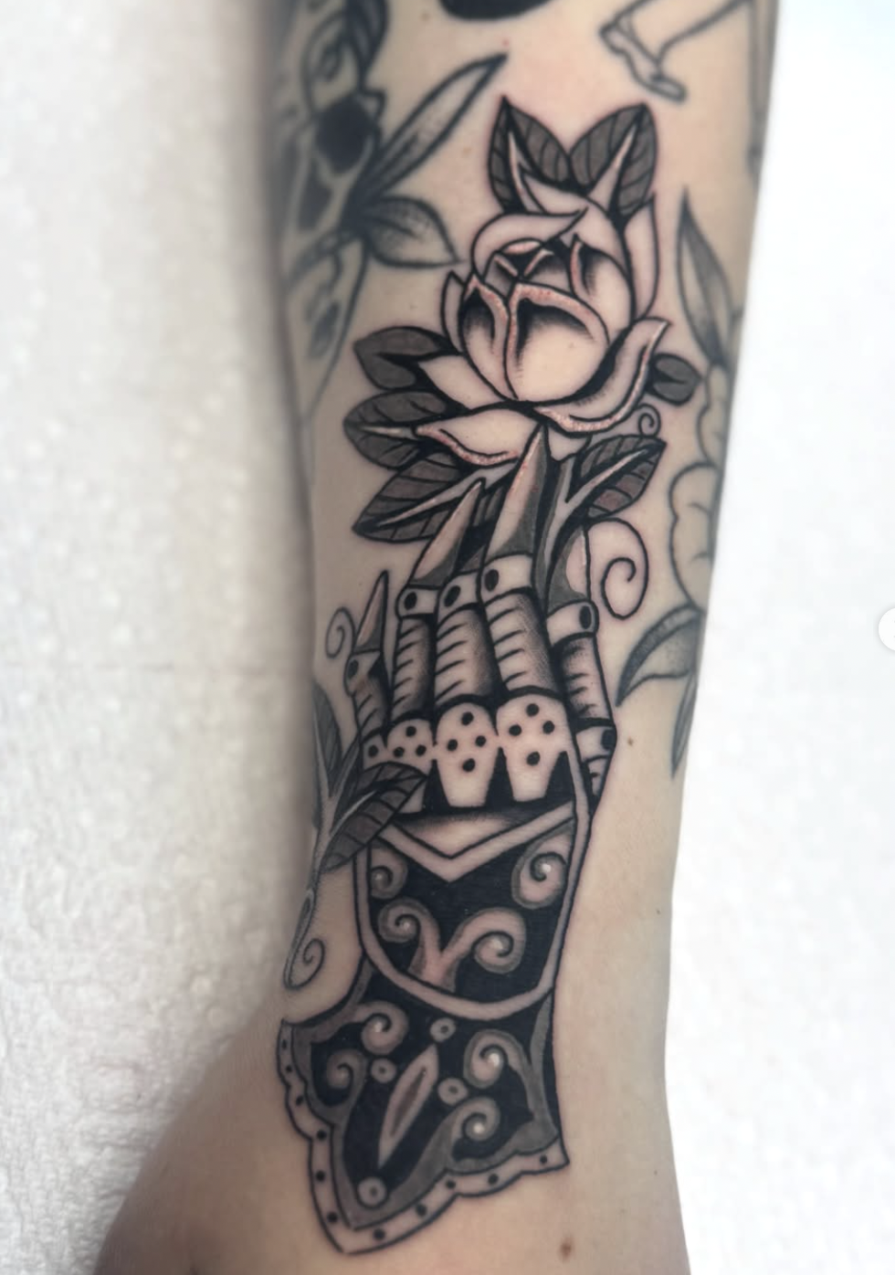 A black tattoo of a mechanical hand holding a rose.