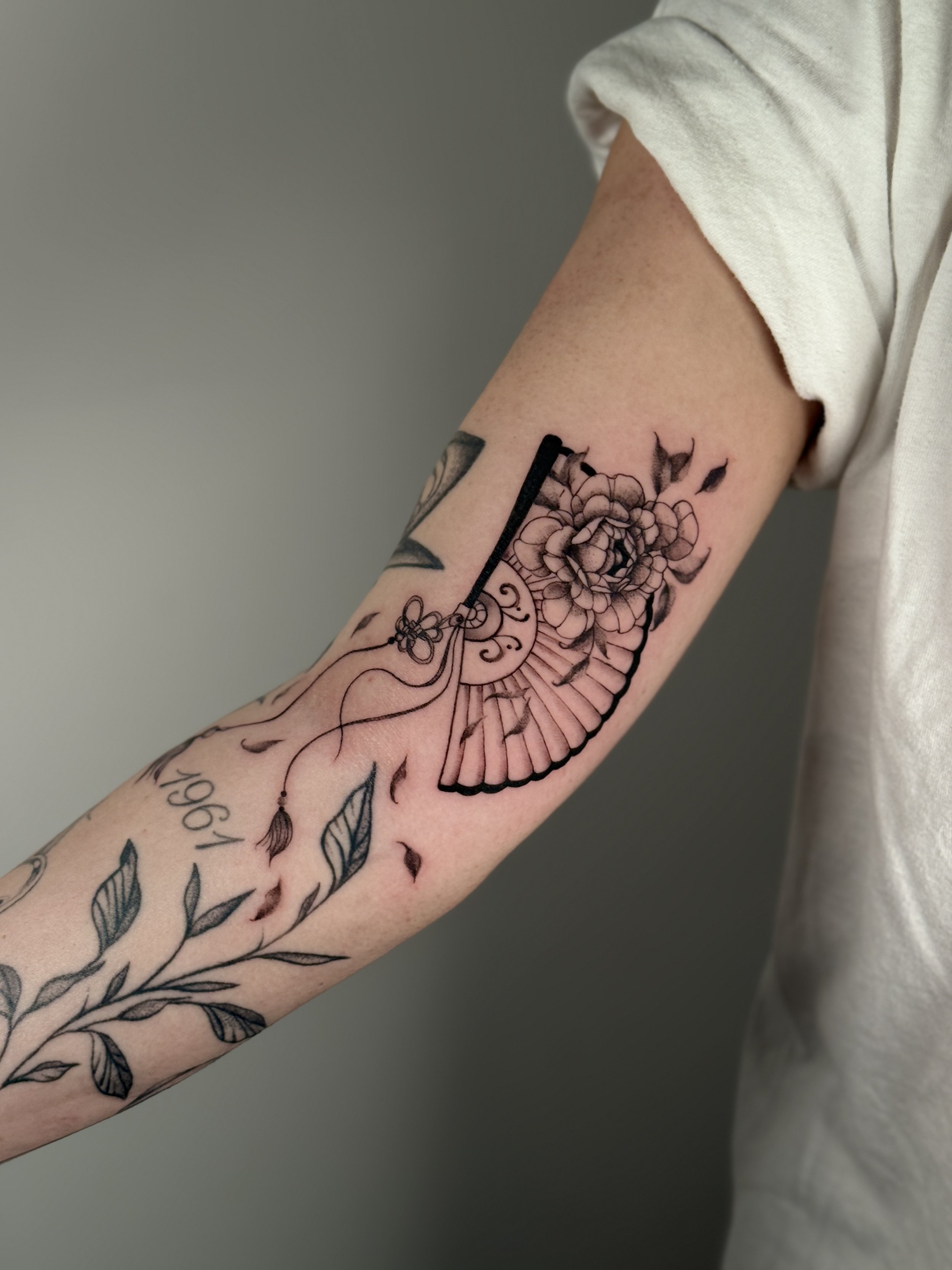 Tattoo of a flower, a clock with numbers, a leaf and a feather on one arm.