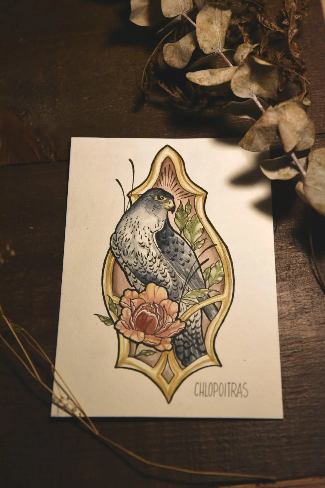 Illustration of a hawk in an artistic tattoo style, framed by a floral decoration with the word "Chlopoitras" written at bottom right.