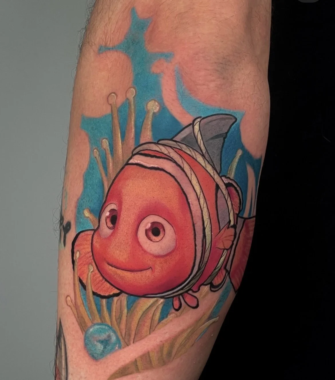 Tatouage d'un poisson clown avec un visage gentil et des couleurs vives, entouré d'éléments marins et de corail.