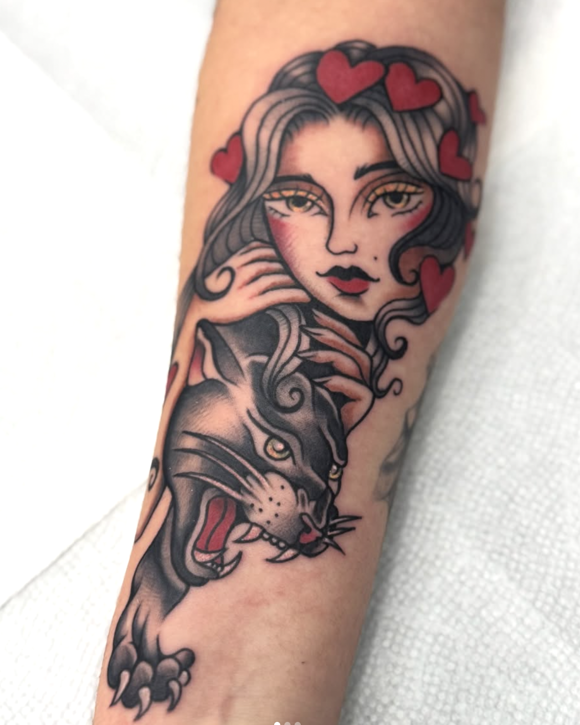 A tattoo of a woman with long, wavy hair, surrounded by red hearts, accompanied by a cartoon-style leopard in black and gray.