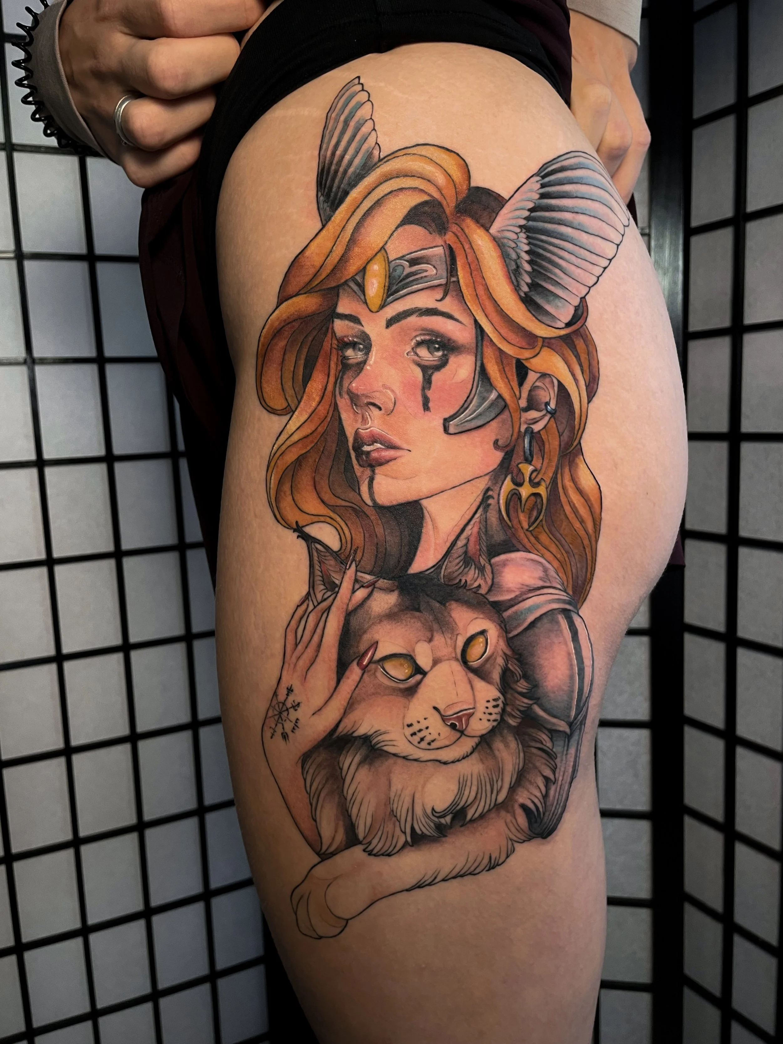 Tatouage d'une femme avec des cheveux roux, une coiffe de guerrière et un maquillage dramatique, accompagnée d'un lion avec des yeux jaunes, le tout en style coloré et détaillé.