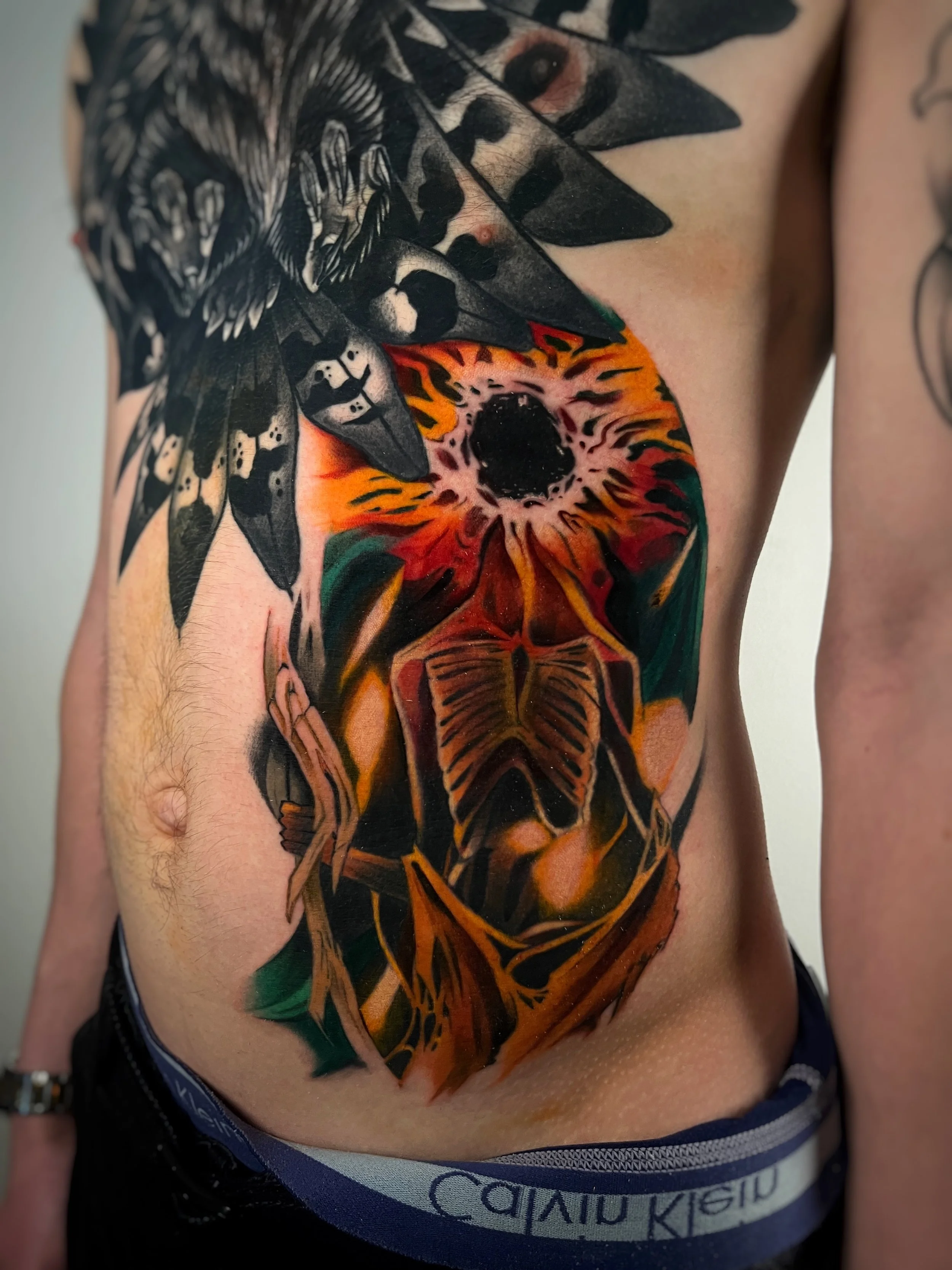 A colorful tattoo depicting a tiger or big cat's head on a man's torso, with black-and-white butterfly designs near the top of the tattoo.