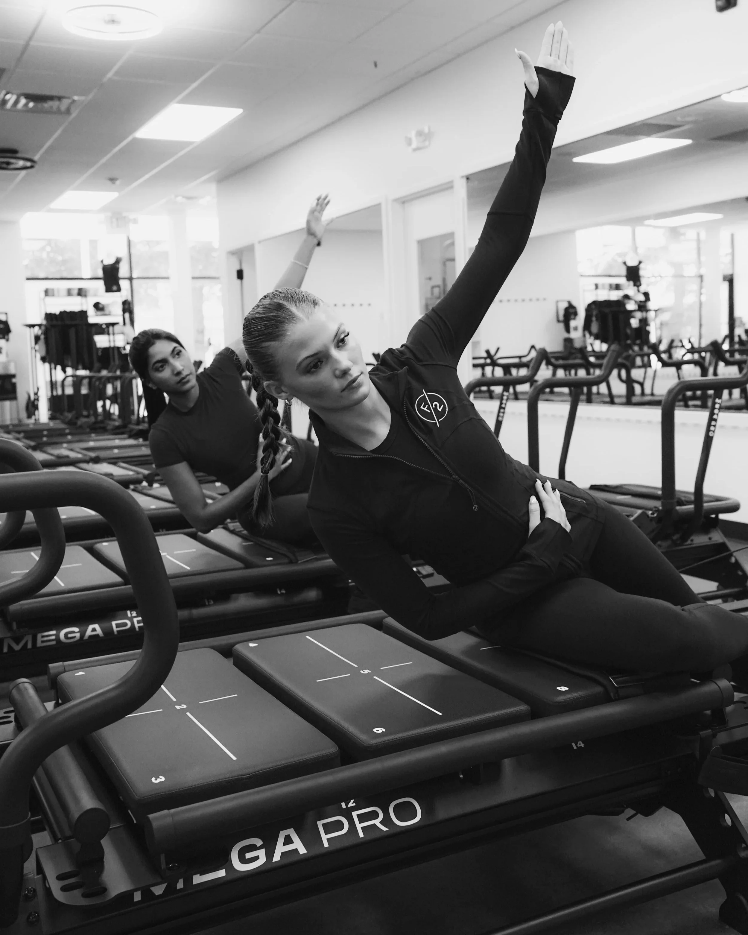 Two women performing side-lying exercises on Megaformers at FORM BY TWO, one in the foreground raising her arm, both focused and in workout attire.