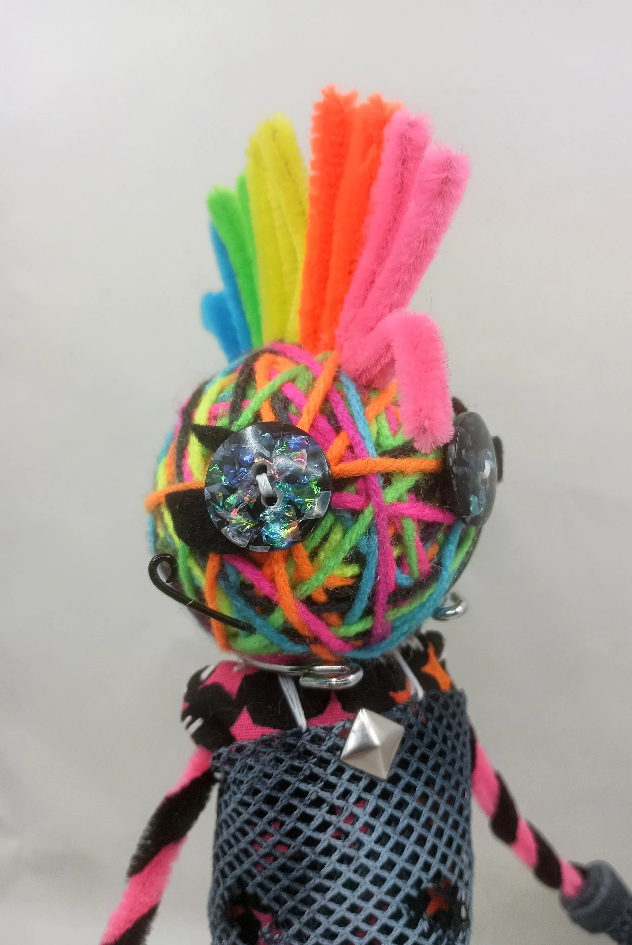 Glamrock Omni Doll Detail, yarn, pipe cleaners, buttons, mesh, faux leather ribbon, 2025
