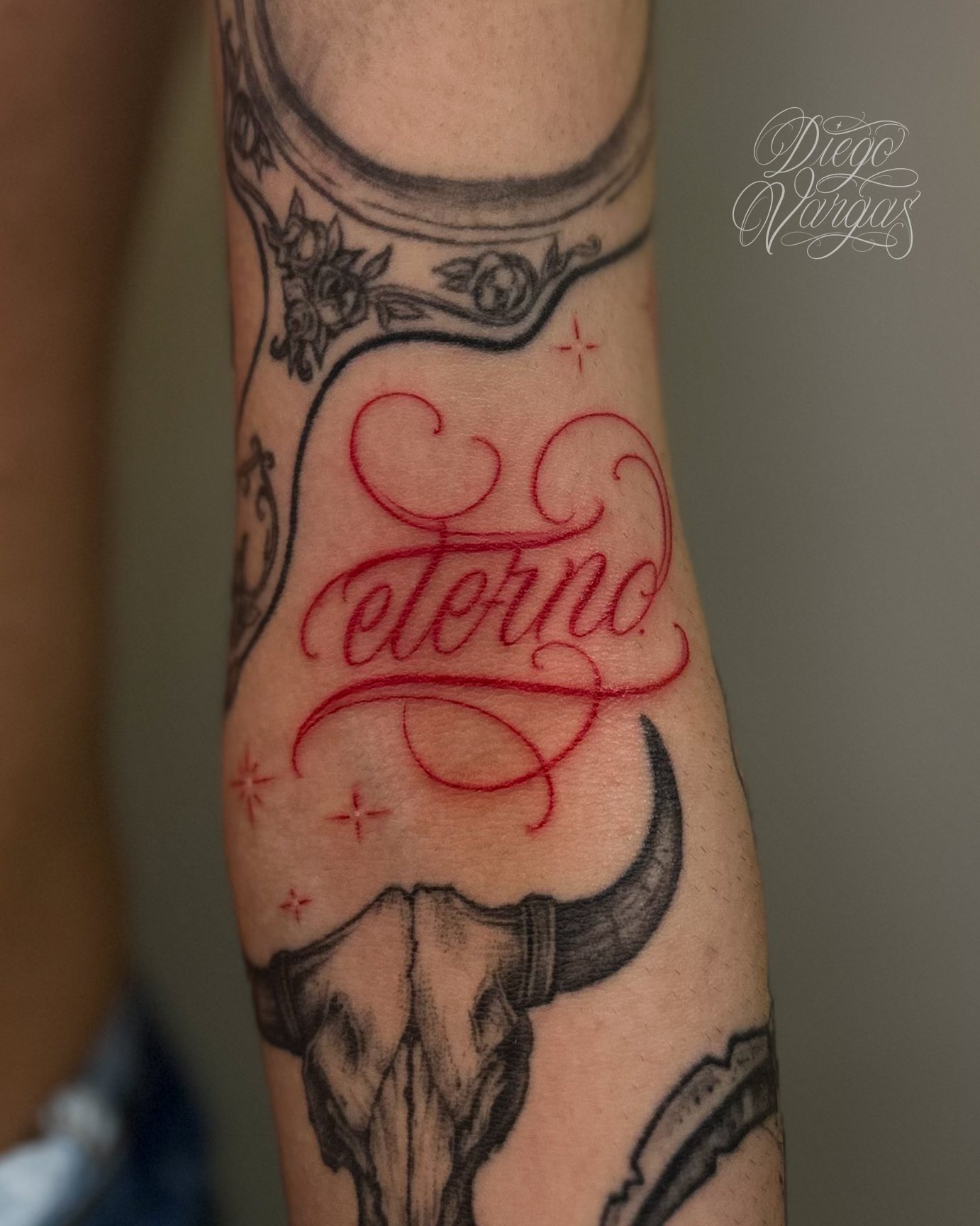 Tattoo of a cow skull with horns and stars, with the red word 'Eterno' written in ornate script.