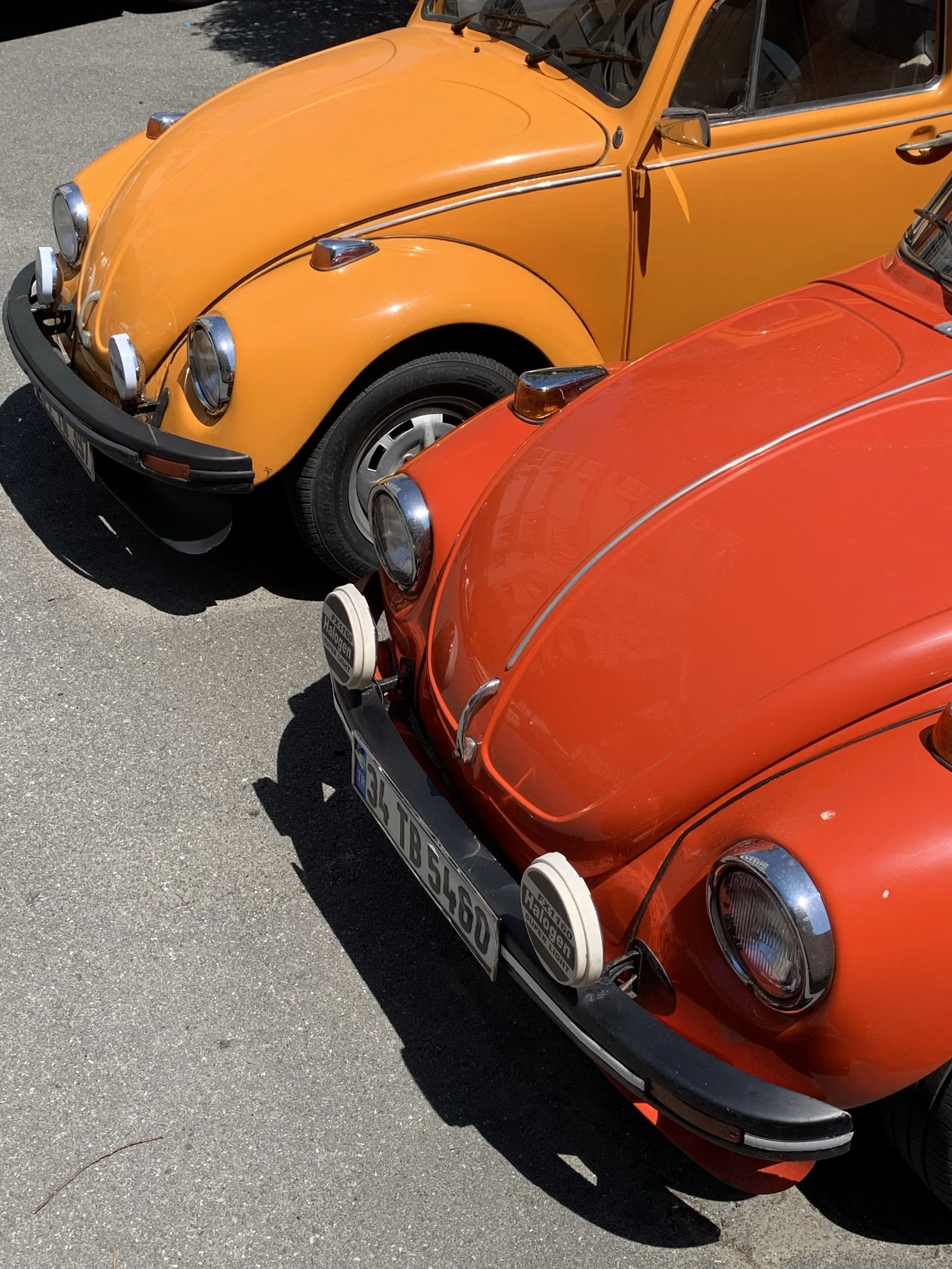 Close-up of two vintage Volkswagen Beetle cars, one orange and one red, parked on a paved surface.