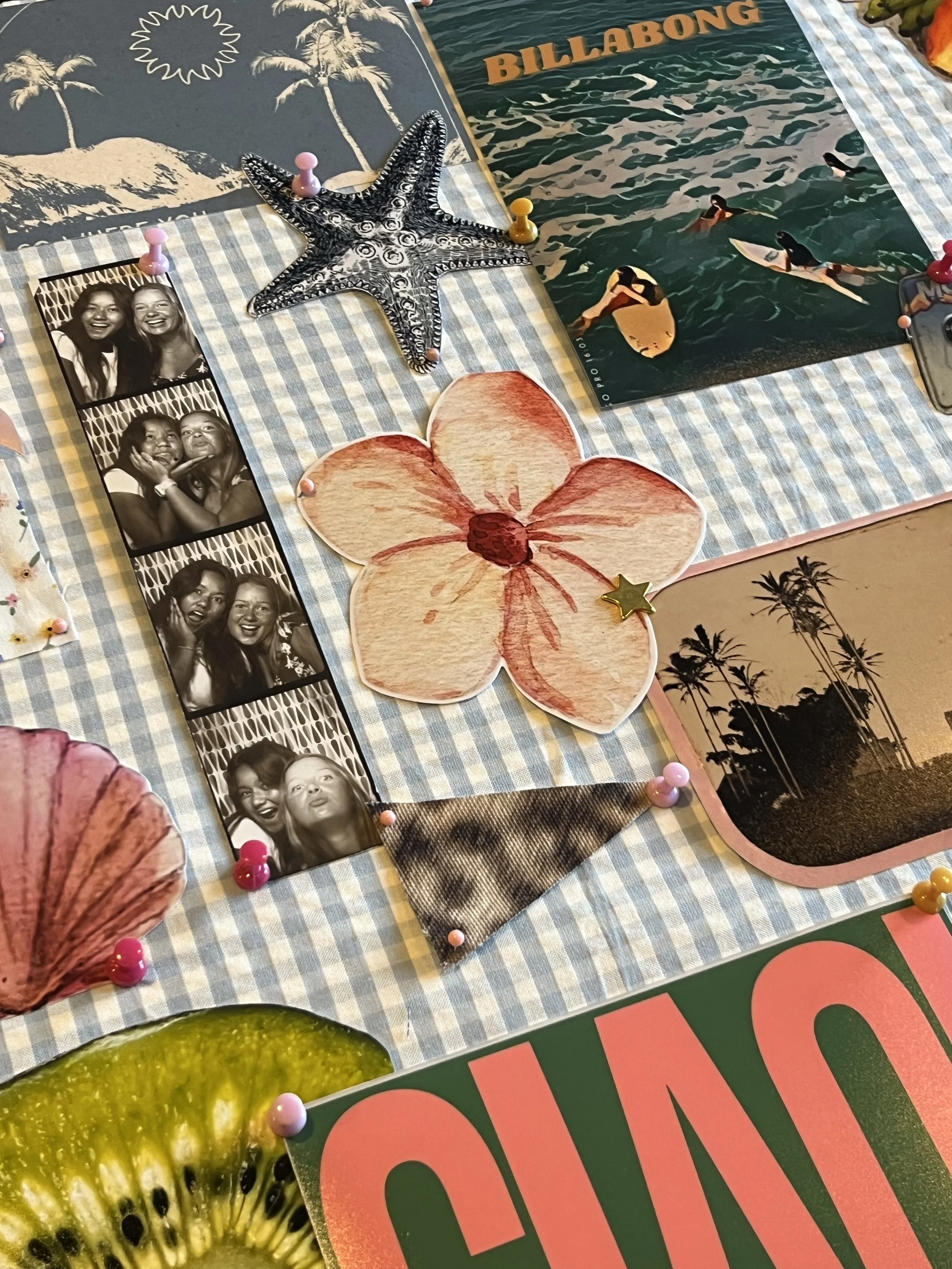 Close-up of a scrapbook page with black and white photo booth strips of two women making funny faces, decorations including a starfish, a large pink and red flower, a poster with surfers at a beach with the word 'Billabong', and a partly visible green kiwi fruit image.