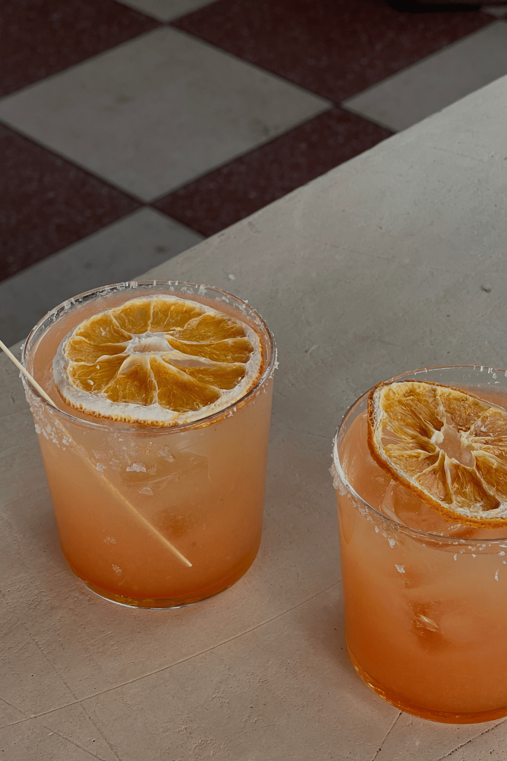Two glasses of orange-colored drinks garnished with orange slices on a white table.