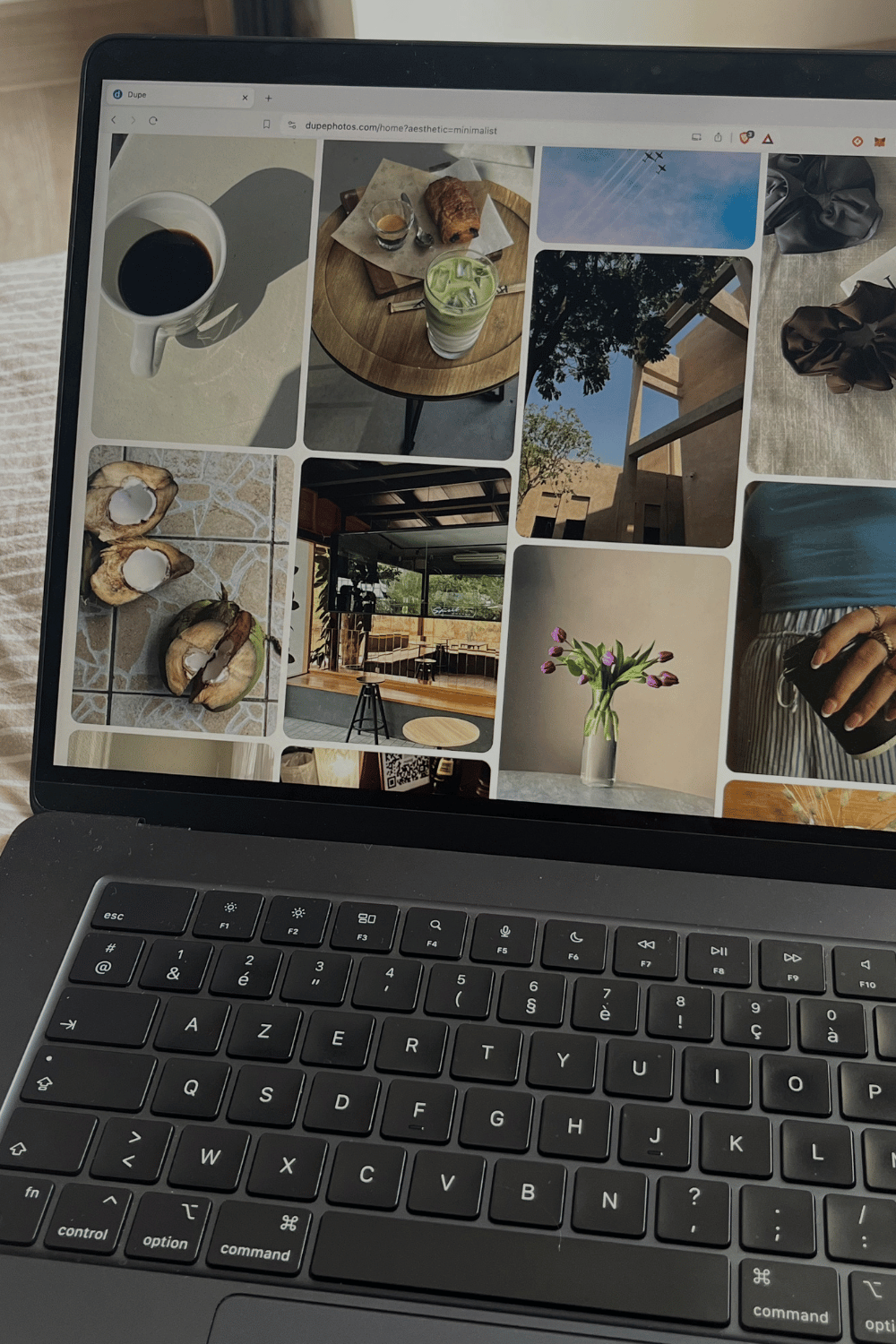 Laptop screen displaying a collage of nine images including a cup of coffee, a pastry and drink on a round table, blue sky with clouds, a tree through a window, a cozy interior with a wooden bar, purple tulips in a vase, a person holding a camera, and some snacks.