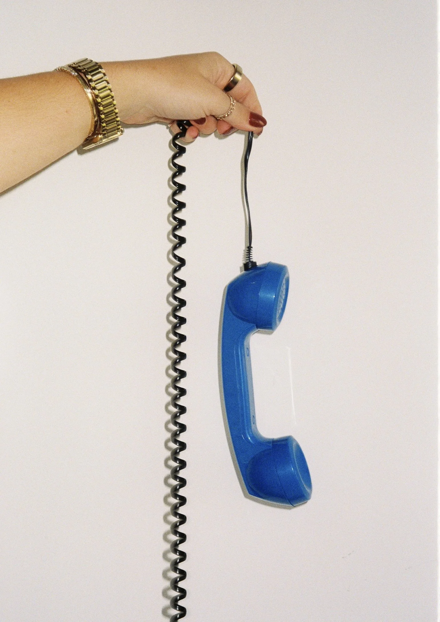 Someone holds a blue wall phone with a coiled cord against a white background.