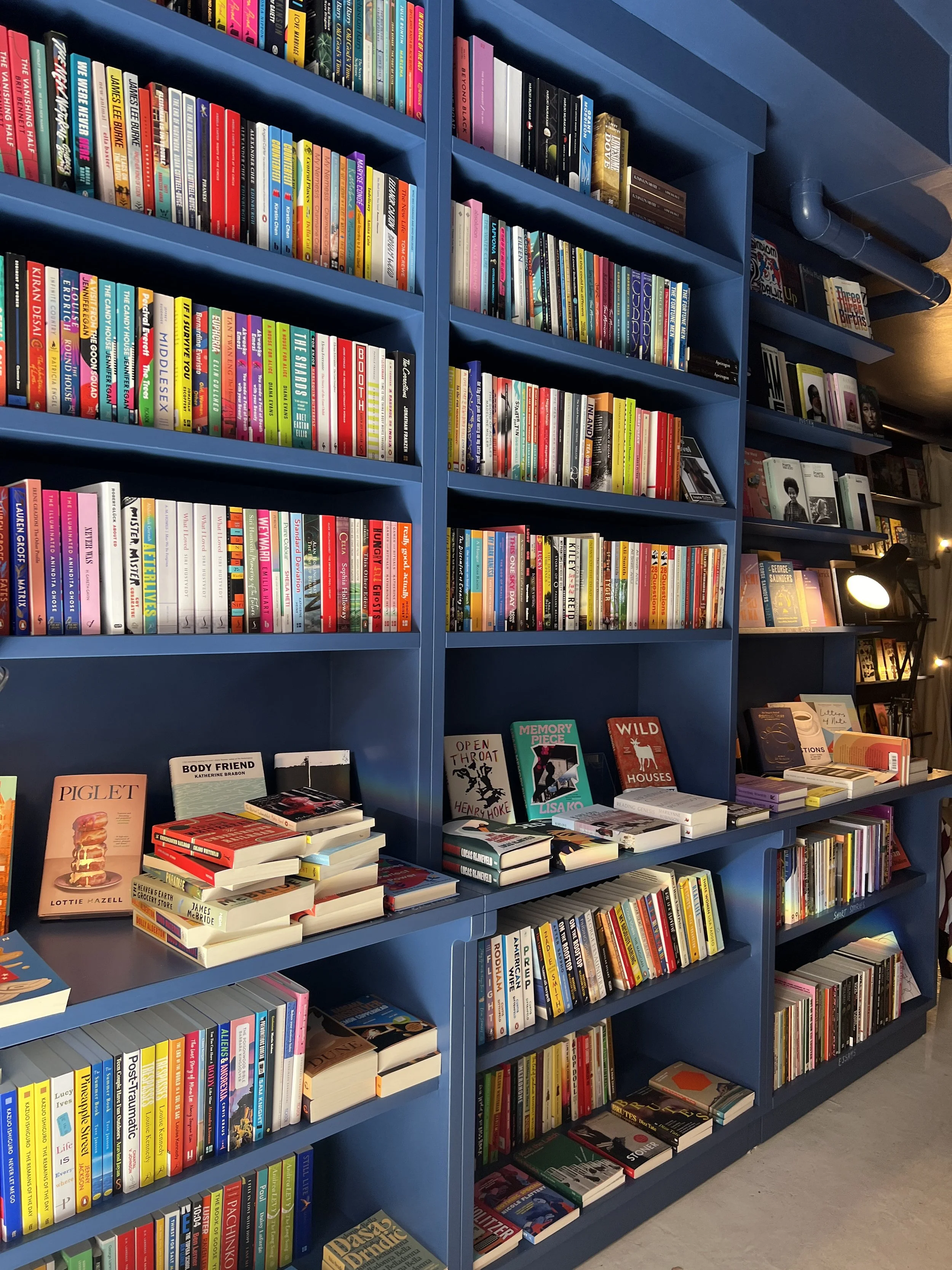 Colorful bookshelves filled with books in a bookstore or library, with a table displaying books on various topics at the front.