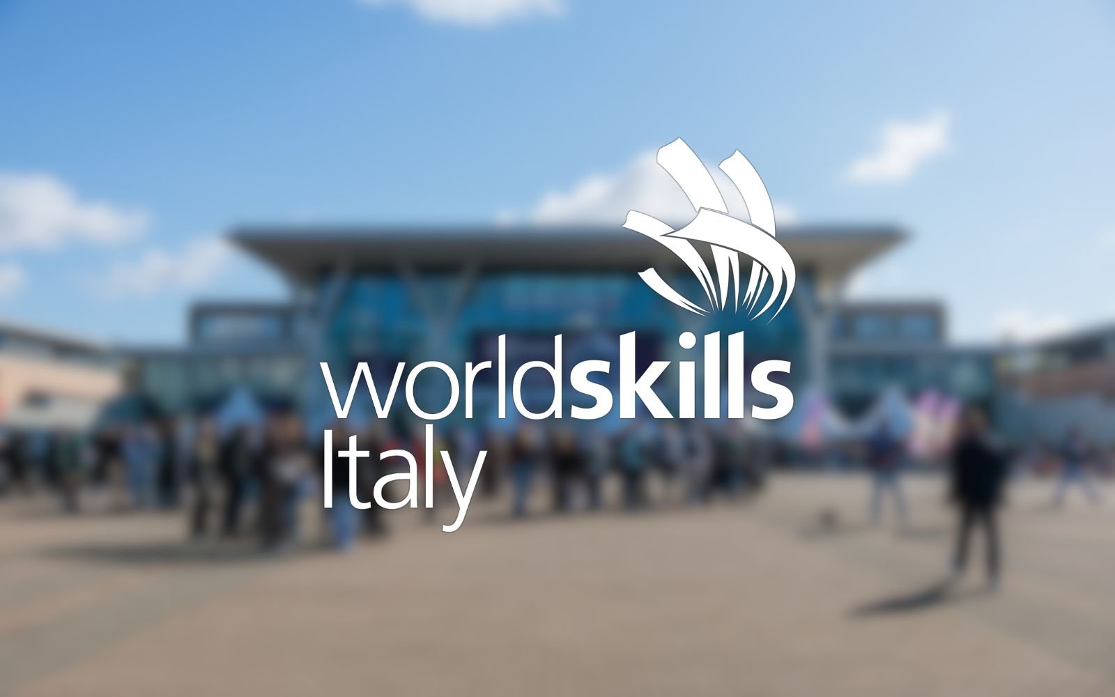 Blurred outdoor scene at WorldSkills Italy event with crowd and exhibition tents, with logo and text overlay for WorldSkills Italy.