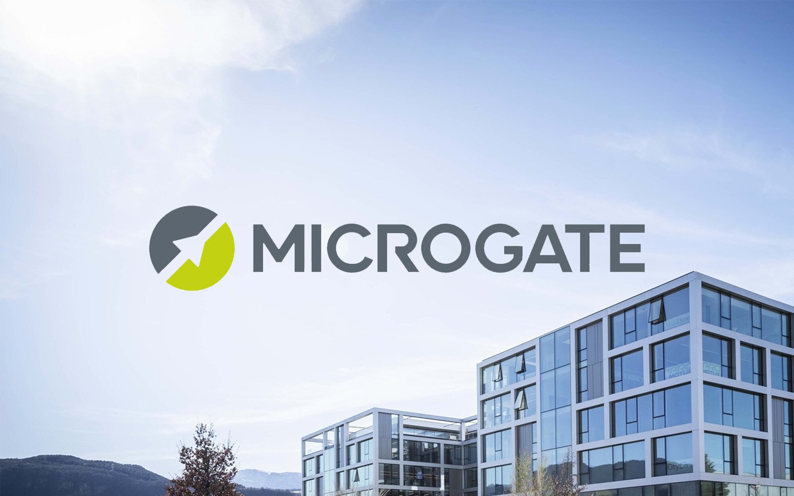 Modern glass office building with mountains in the background and the MICROGATE logo overlayed.