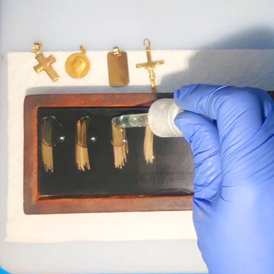 Procedimiento con una pipeta y objetos dorados, cruces, monedas y una caja con viales.