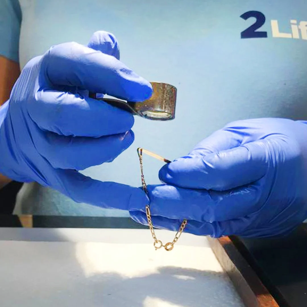 Manos con guantes de látex dorados usando un microscopio y un pincel para manipular un pequeño objeto.