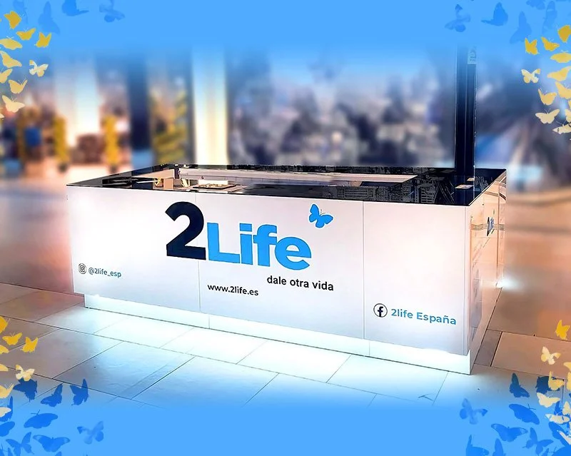 Mostrador con el logotipo de 2Life y el lema 'dale otra vida', decorado con mariposas azules y amarillas.