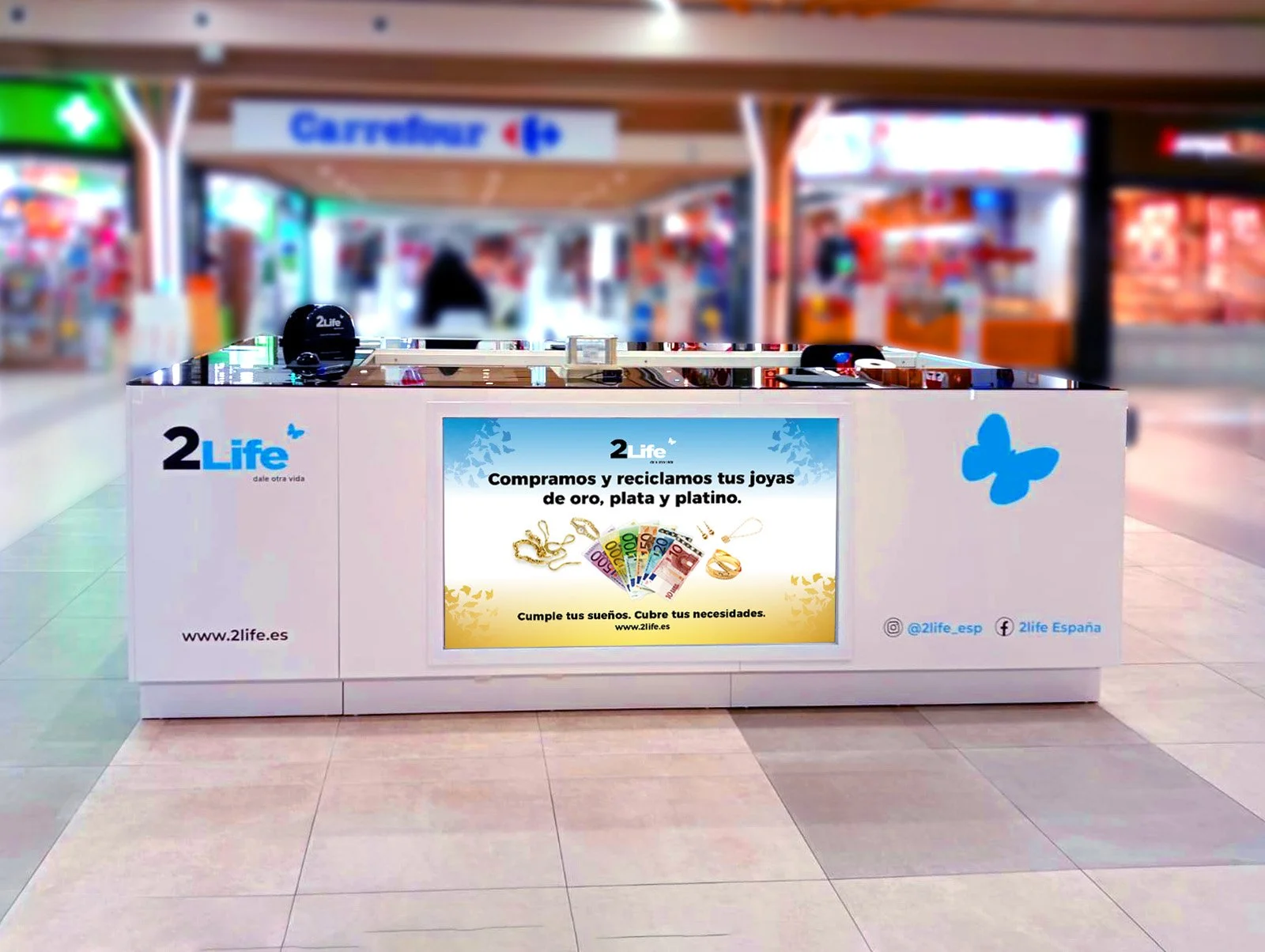 Puente de compra de joyas en un centro comercial con cartel que dice 'Compramos y reciclamos tus joyas de oro, plata y platino', y muestra imágenes de billetes y joyas, con fondo difuso de tiendas.