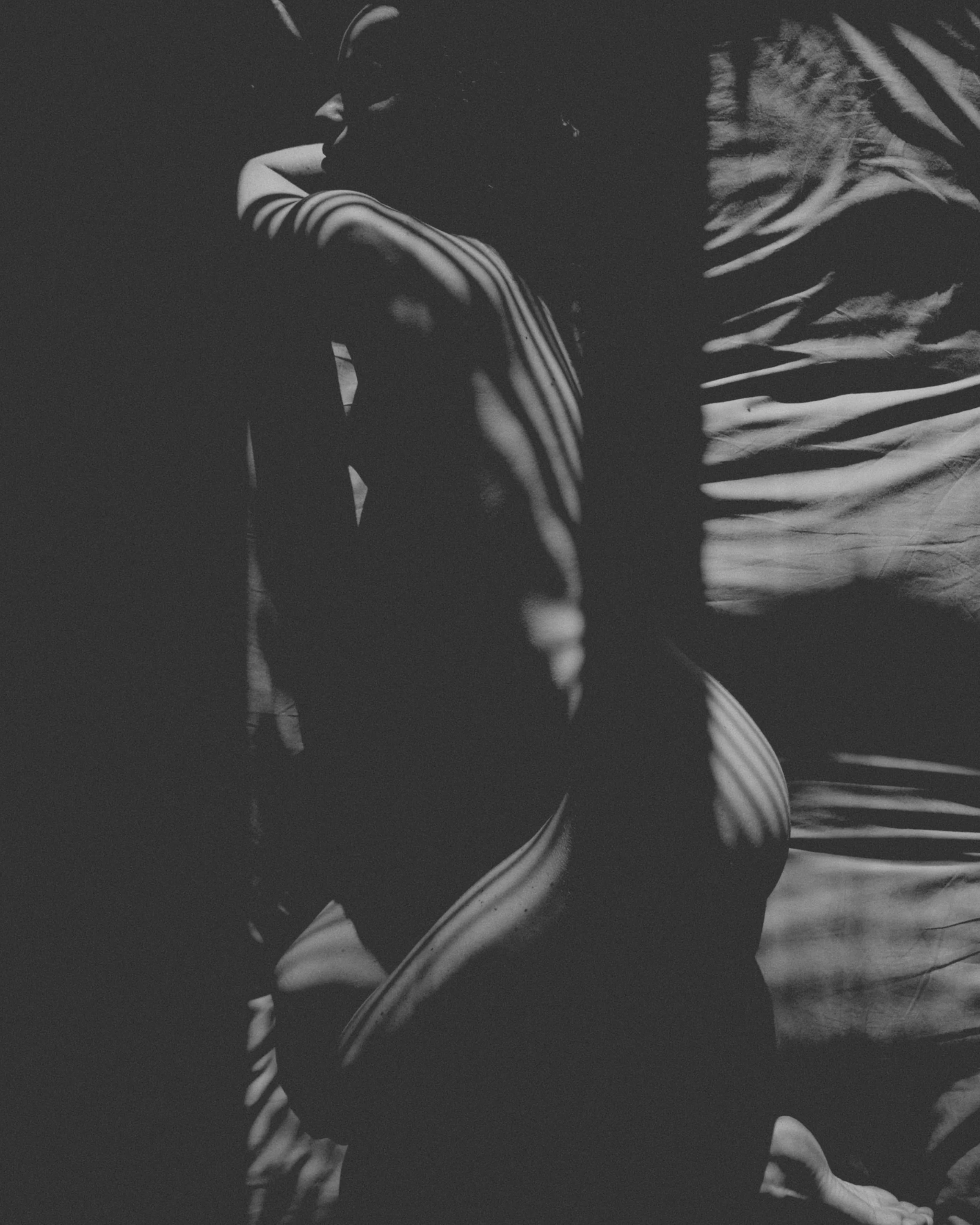Schwarz-Weiß-Foto einer Frau auf dem Boden in Schatten, mit Lichtstrahlen, die entlang ihres Körpers und ihrer Kleidung fallen.