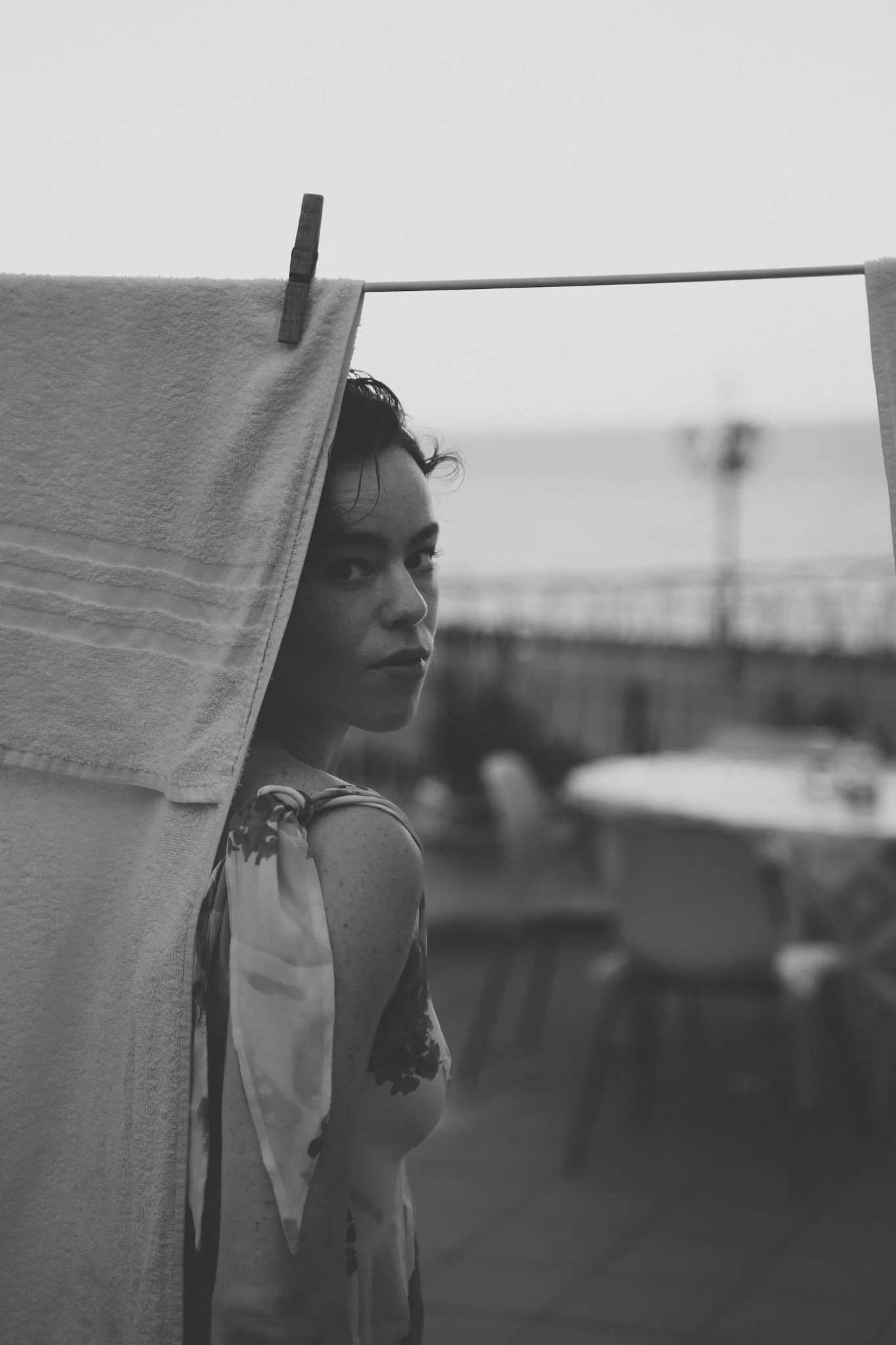 Frau schaut hinter einer Wäscheleine hindurch, im Hintergrund der Strand und das Meer, in schwarz-weiß.