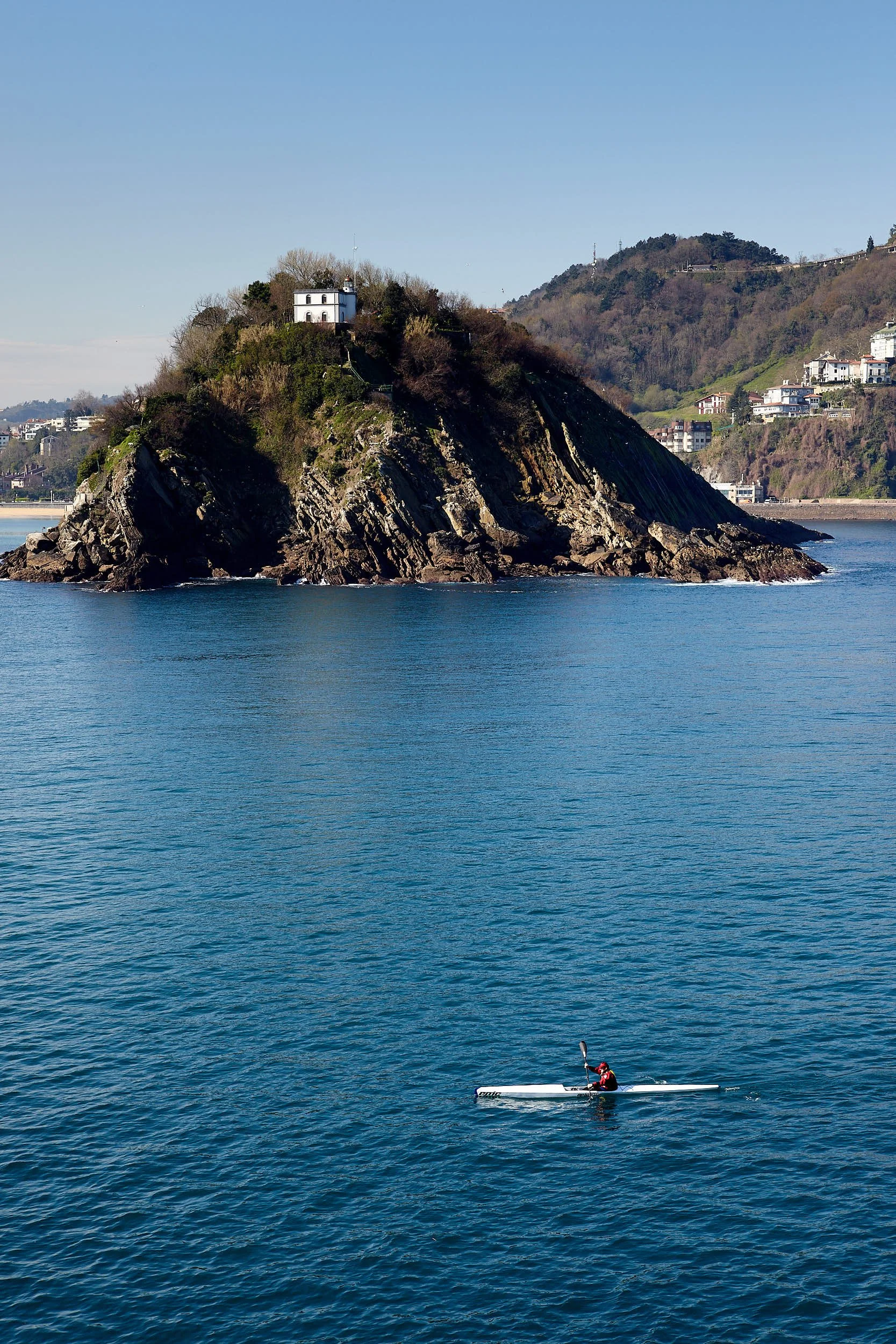 Canoeist heading back to harbour, passing St Clara island, San Sebastián, Gipuzkoa, Basque Country, Spain.