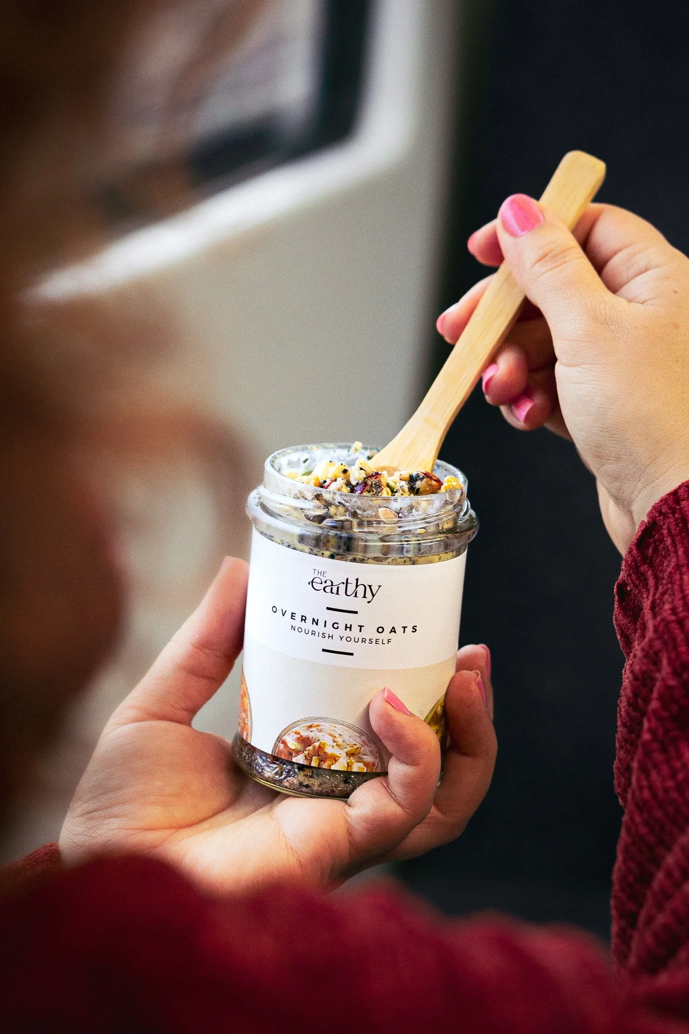 A person holding a jar of The Earthy overnight oats with a wooden spoon, eating the oats on a train. Kathleen Gillan Photography copyright-protected.