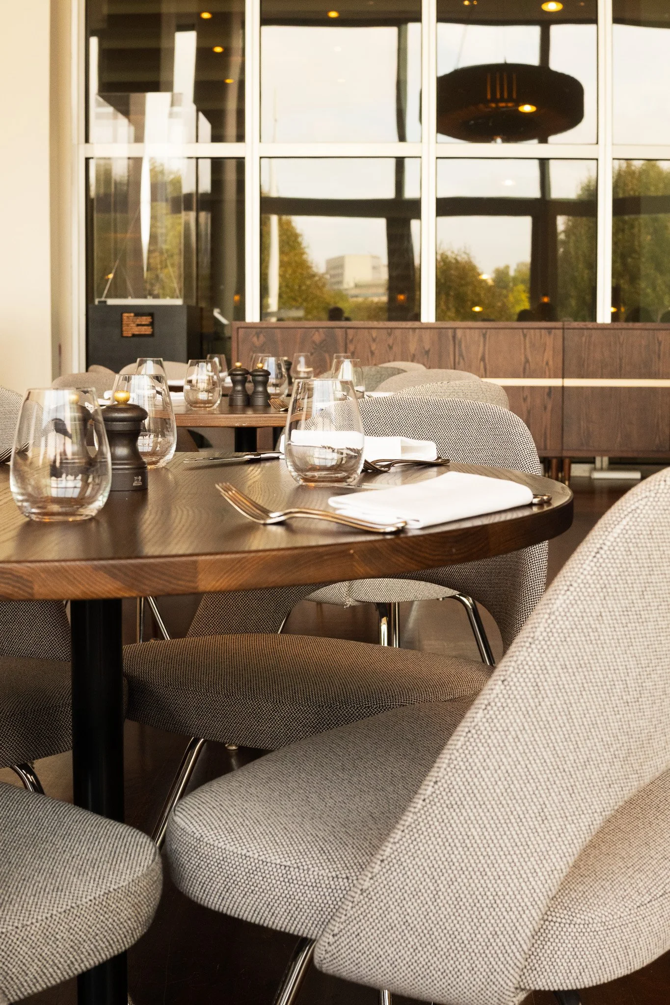 Prepared restaurant table at The Skylon restaurant, in the Royal Festival Hall, London, set with water glasses, napkins, silverware, and salt and pepper shakers, near large windows.