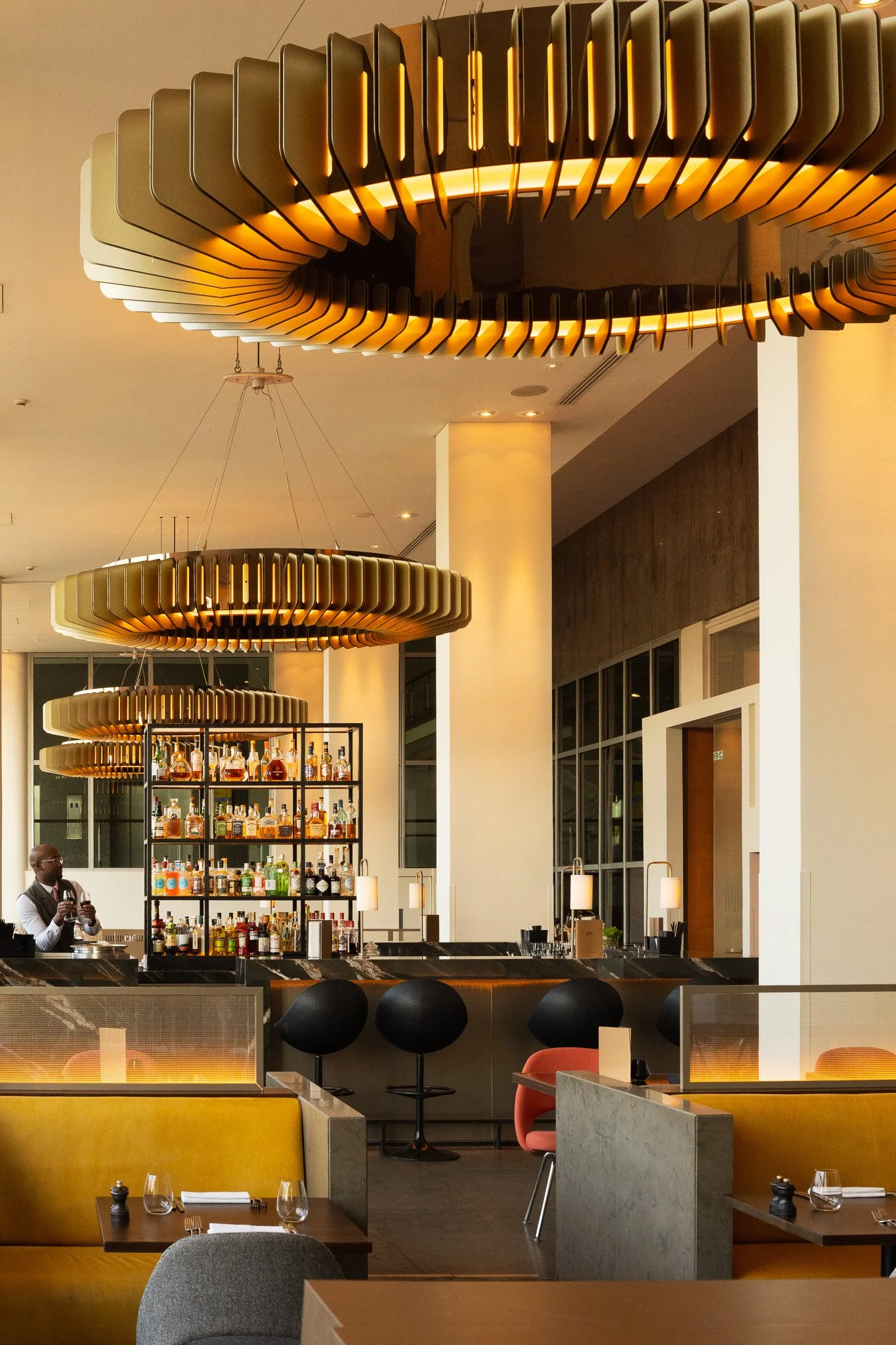 Modern restaurant interior at The Skylon restaurant, in the Royal Festival Hall with bar, shelves of liquor bottles, stylish black and orange chairs, and large circular hanging light fixtures.