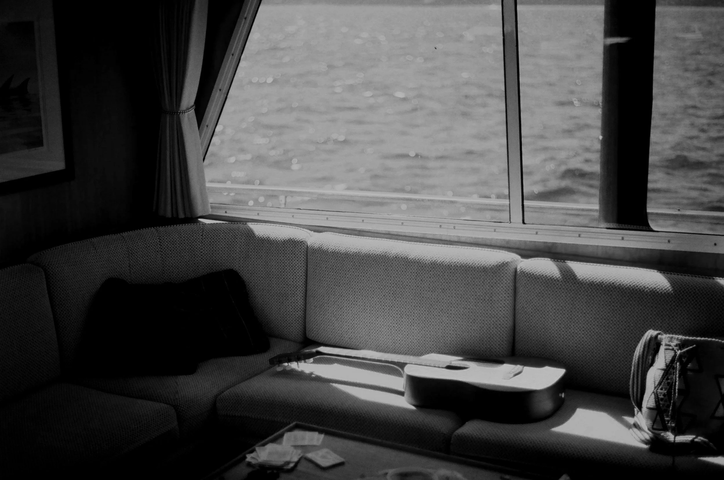 Interior of a boat with a sofa, guitar, and a window showing the water outside.
