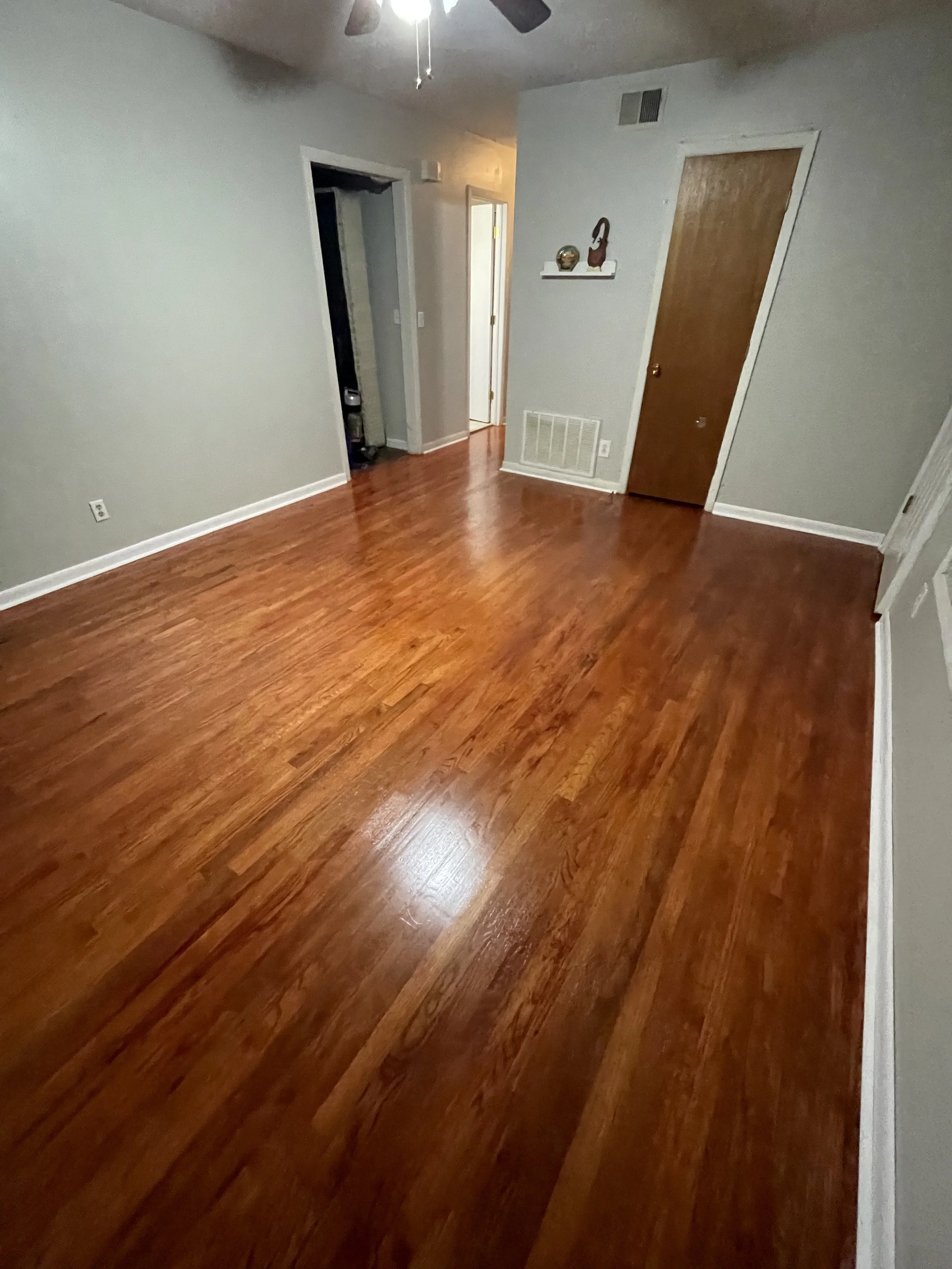 Empty room with hardwood floors, gray walls, a ceiling fan, and a door.