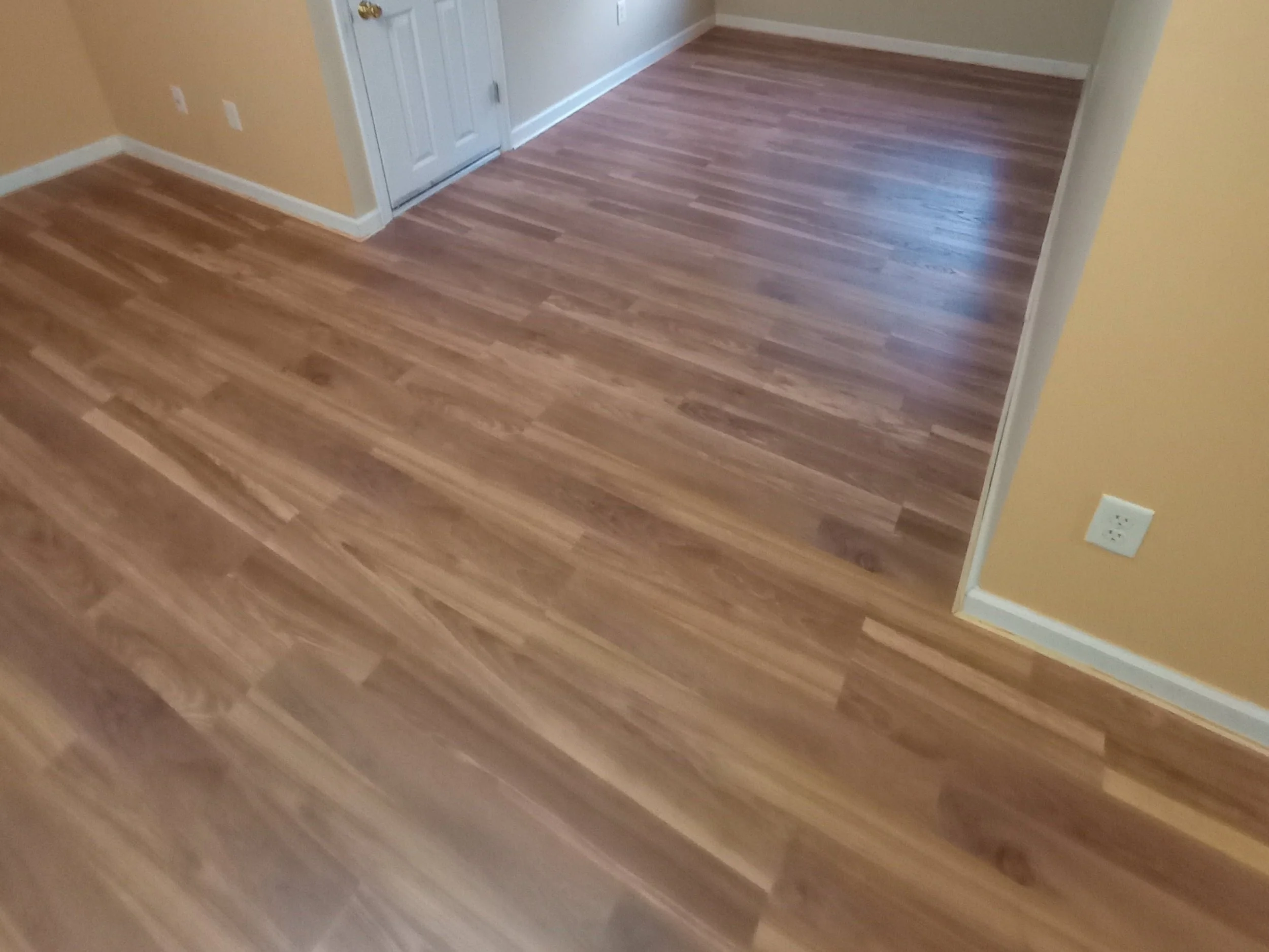 Room with wooden flooring, beige walls, white baseboards, and a white door.