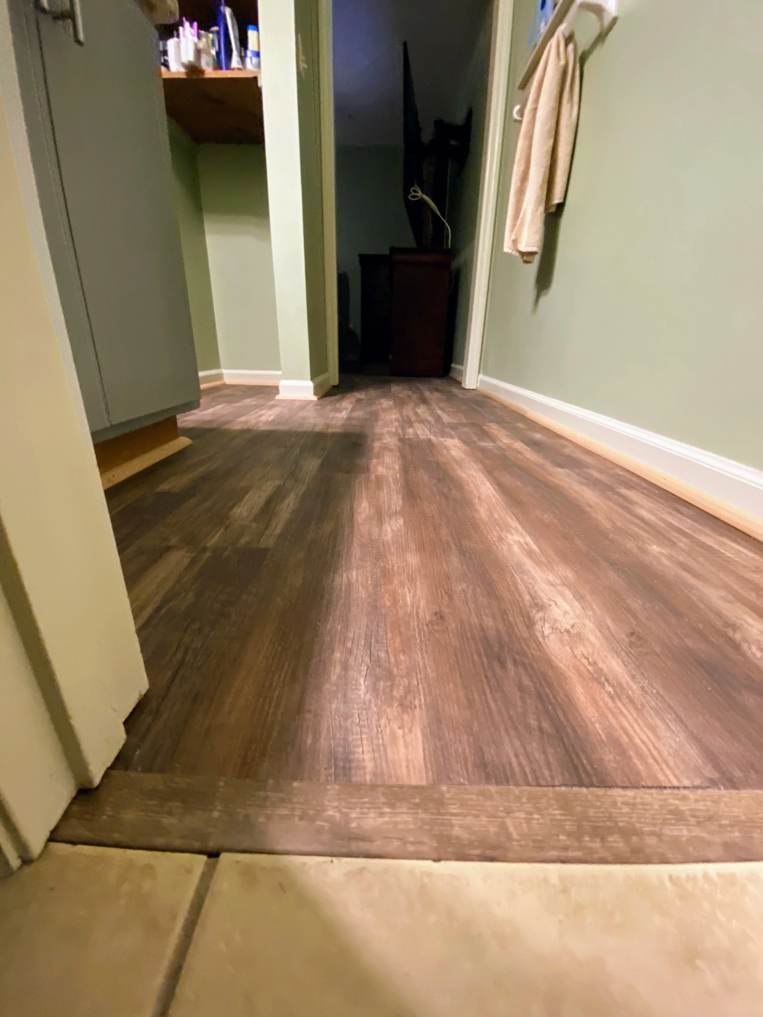 Wood floor transition area between tiled and hardwood flooring in a hallway, with a towel hanging on the wall.